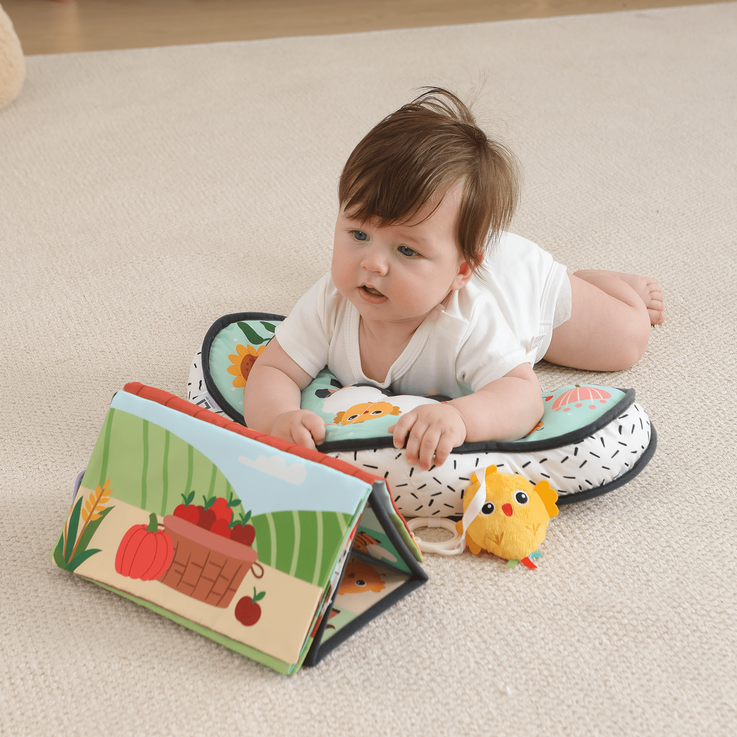 Baby doing tummy time on a support pillow with a farm mirror book and chick rattle