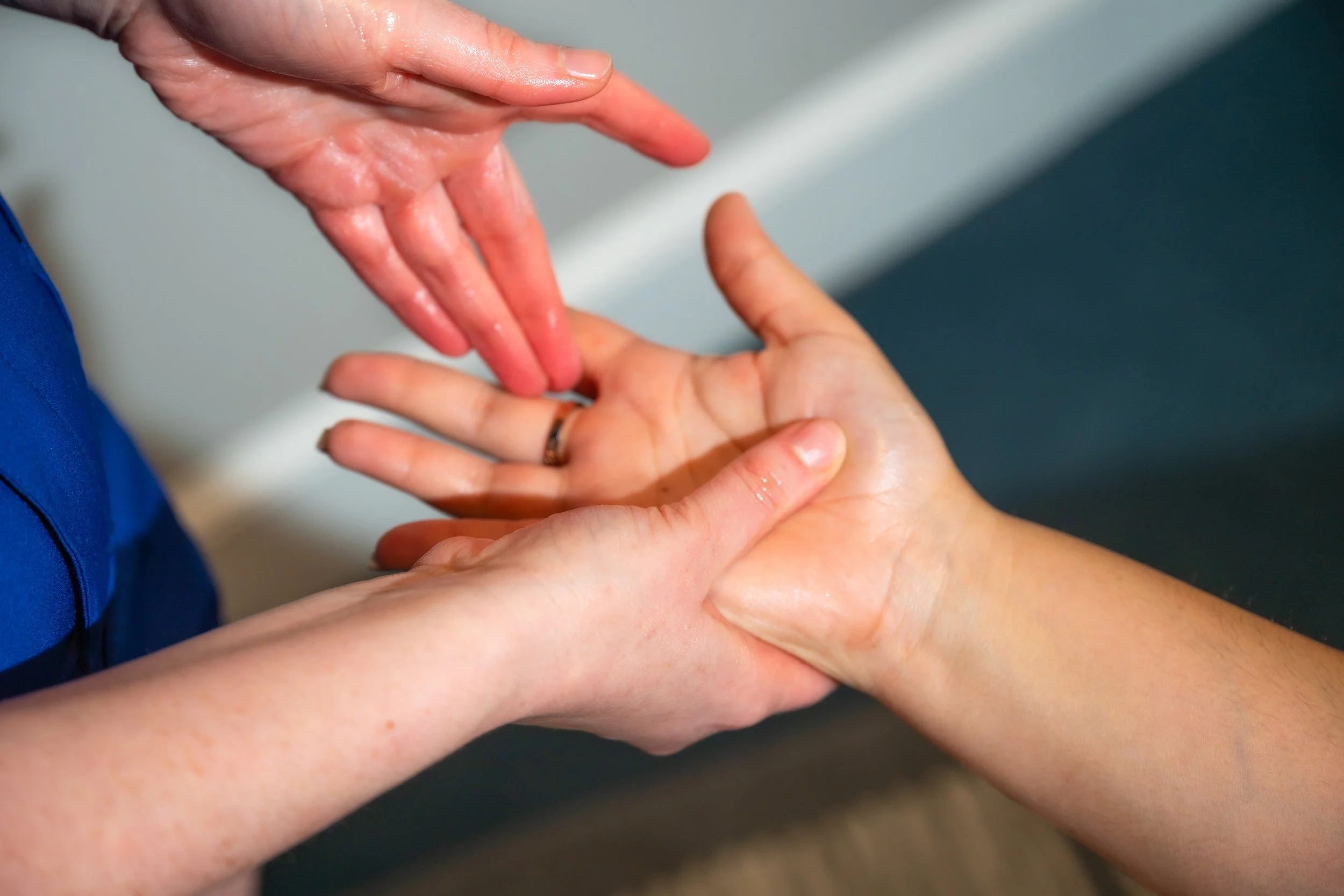 The image shows two individuals holding hands, with one hand providing a massage or therapy to the other. The setting appears to be clinical or therapeutic, with focus on the hands and their interaction.