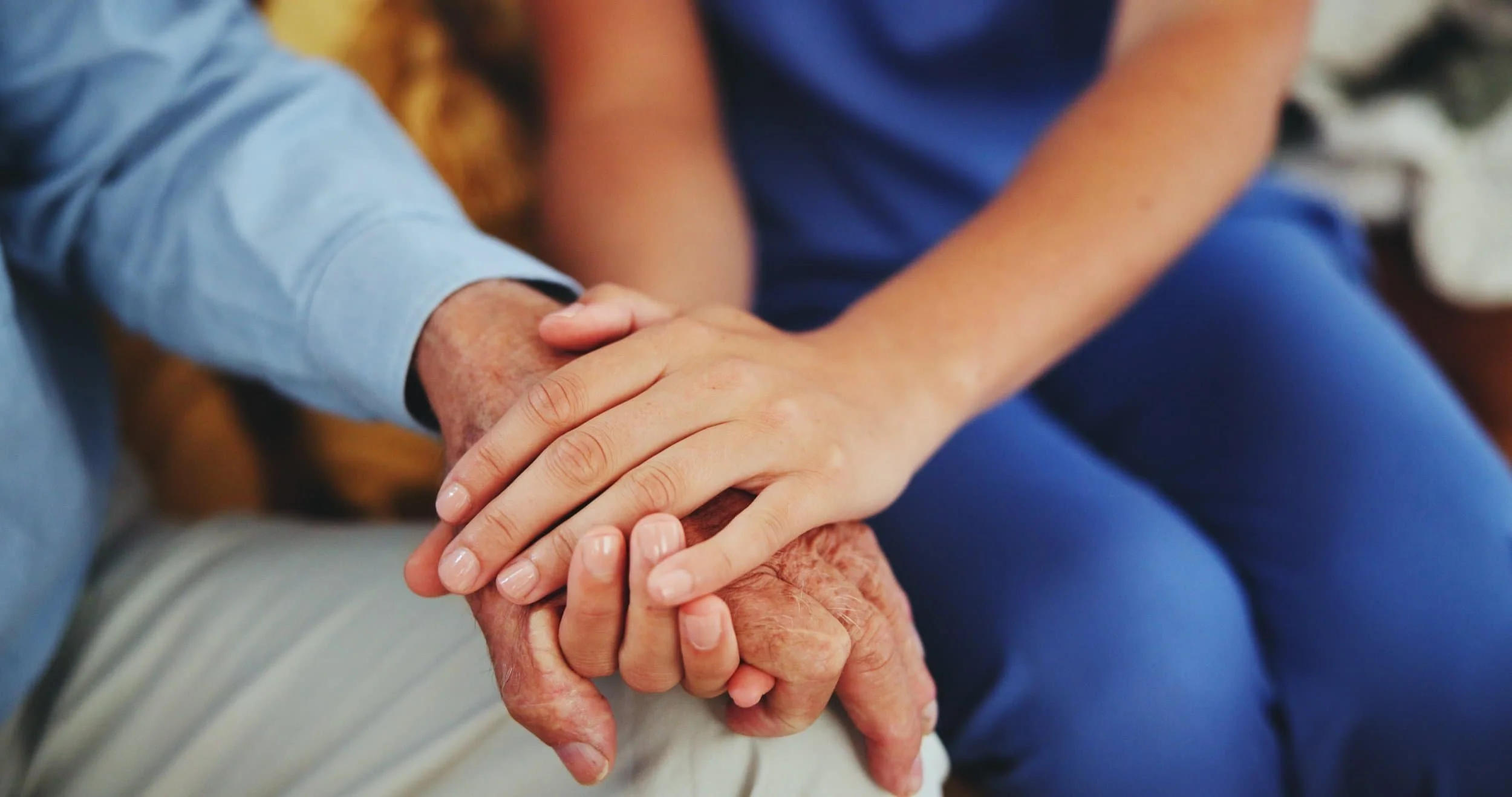 Close-up of two people holding hands, one appears older with wrinkled skin, and the other has smooth skin, indicating caring or support.