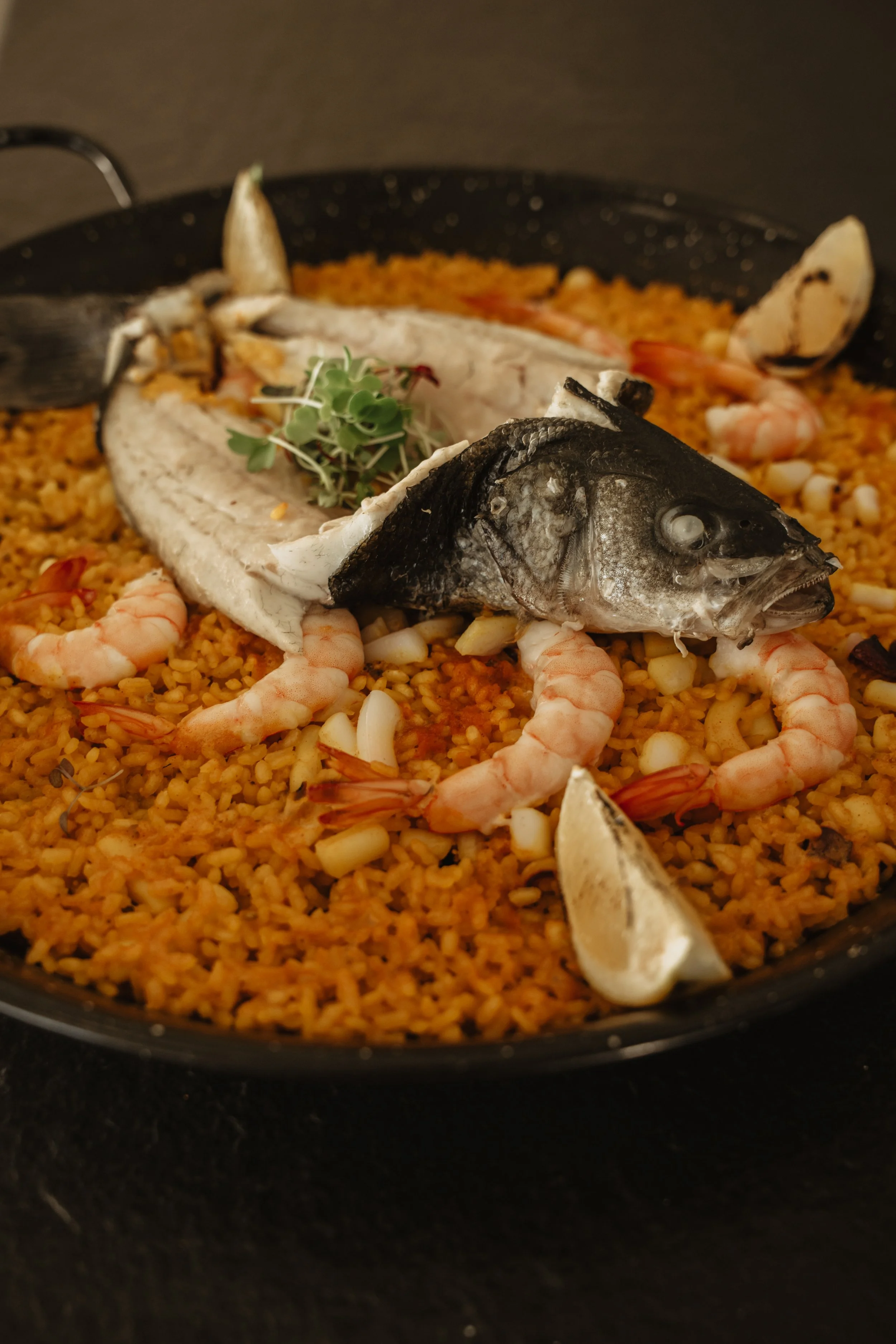 A seafood paella with cooked fish, shrimp, lemon wedges, and rice.