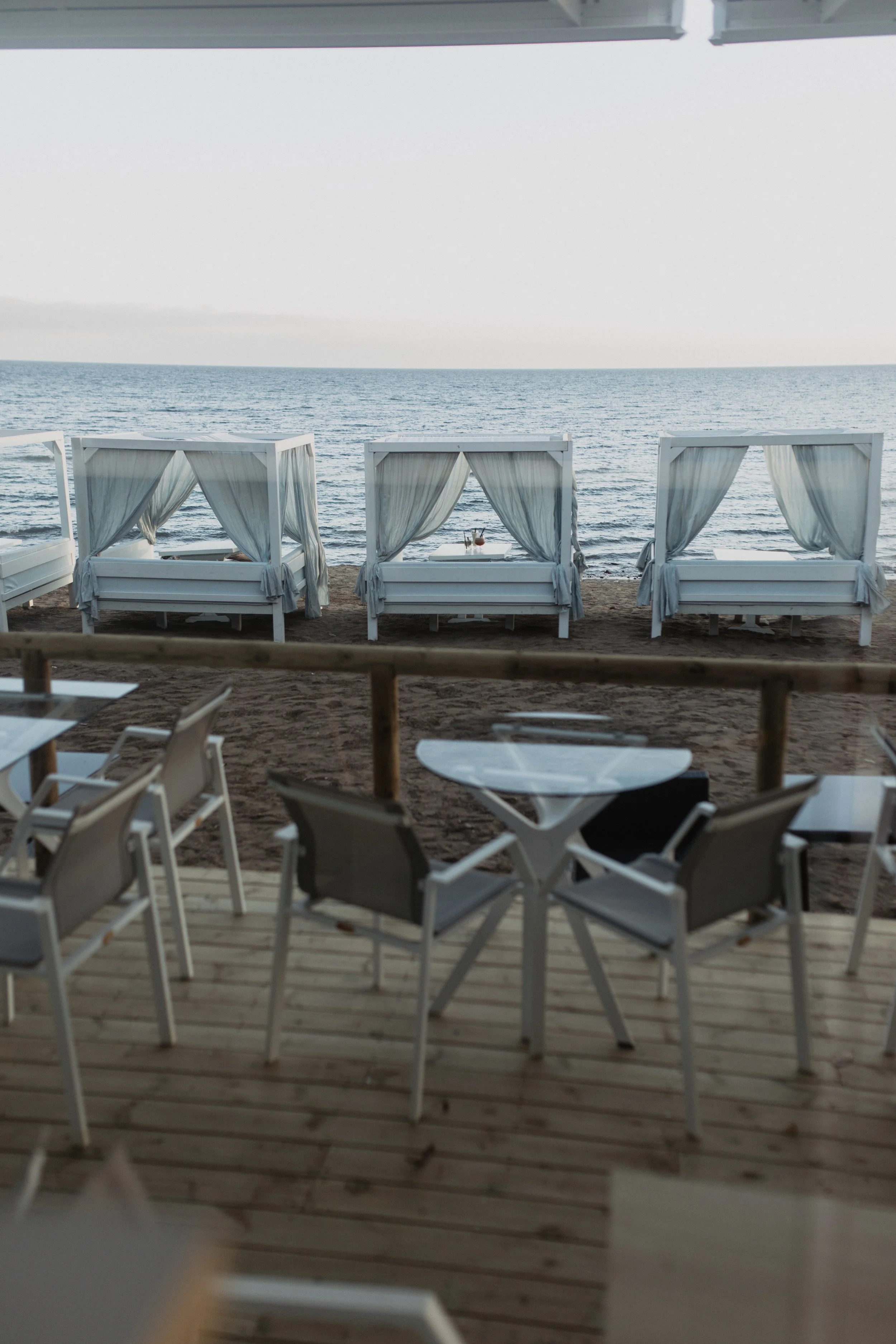 Beachside seating area with white canopy beds and curtains overlooking the ocean.