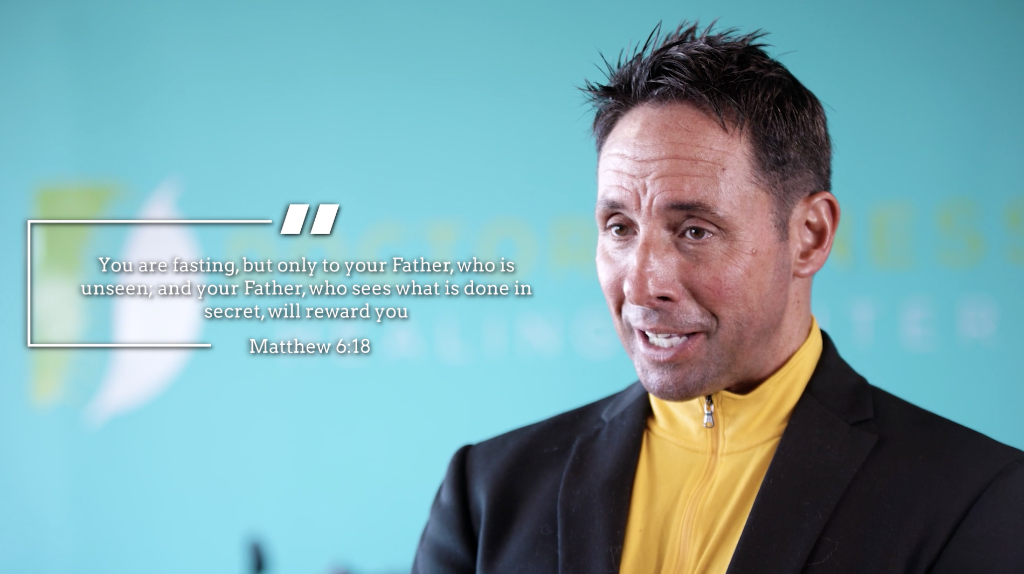 A man in a black suit and yellow shirt speaking with a quote from Matthew 6:18 displayed beside him. The background is light blue with some text and logo faintly visible.