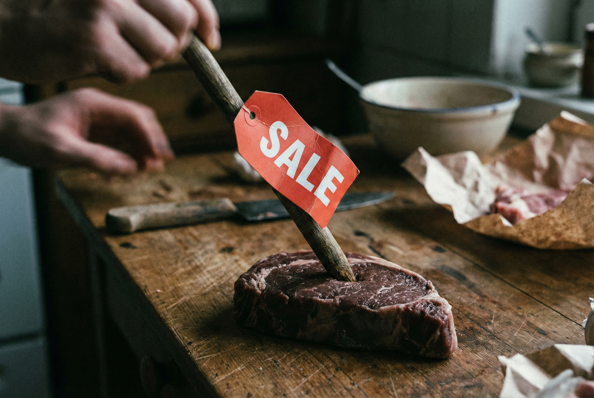 Étiquette de solde rouge plantée dans de la viande crue, symbolisant l'instinct de prédation du consommateur.
