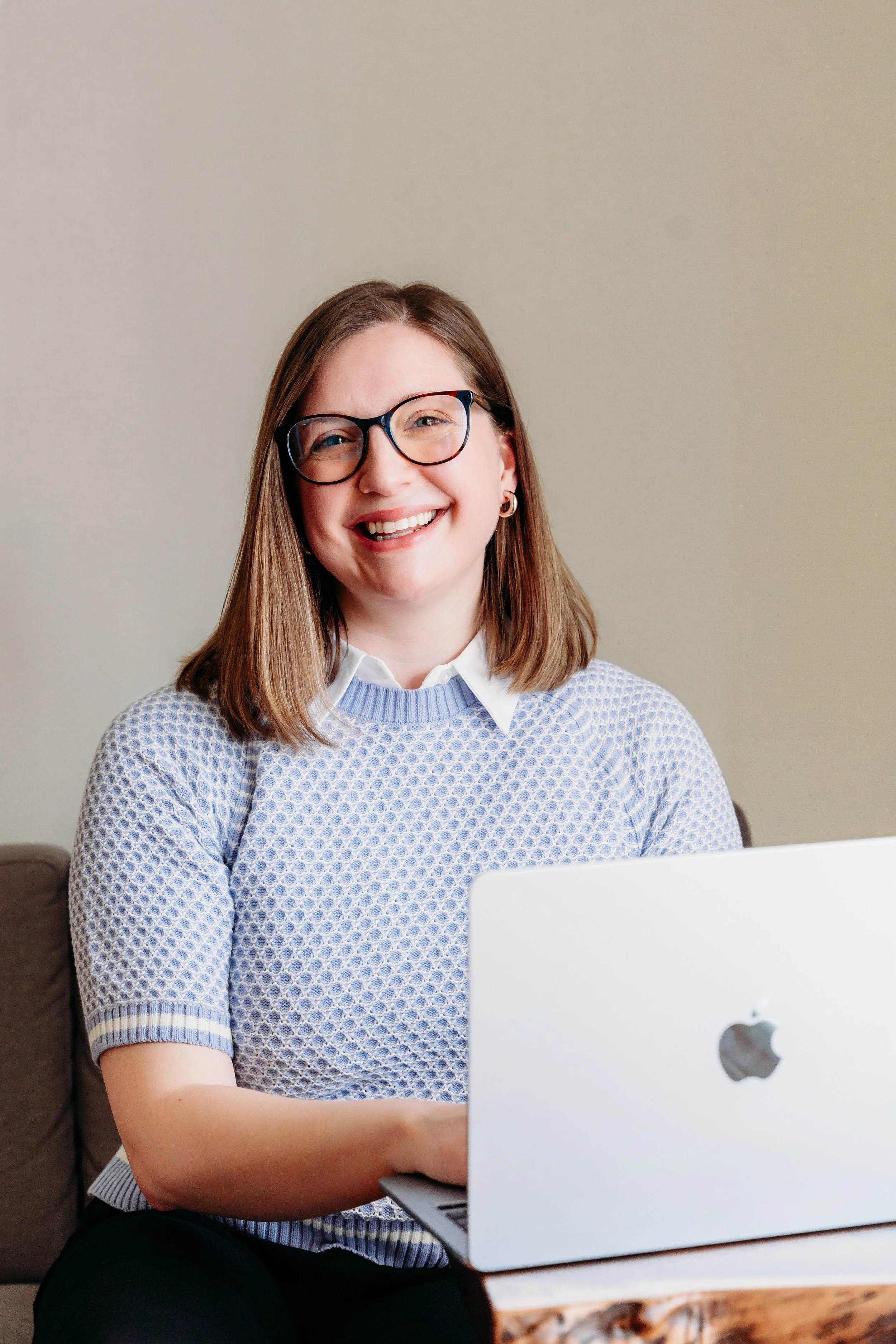 A smiling woman wearing glasses working on a laptop.