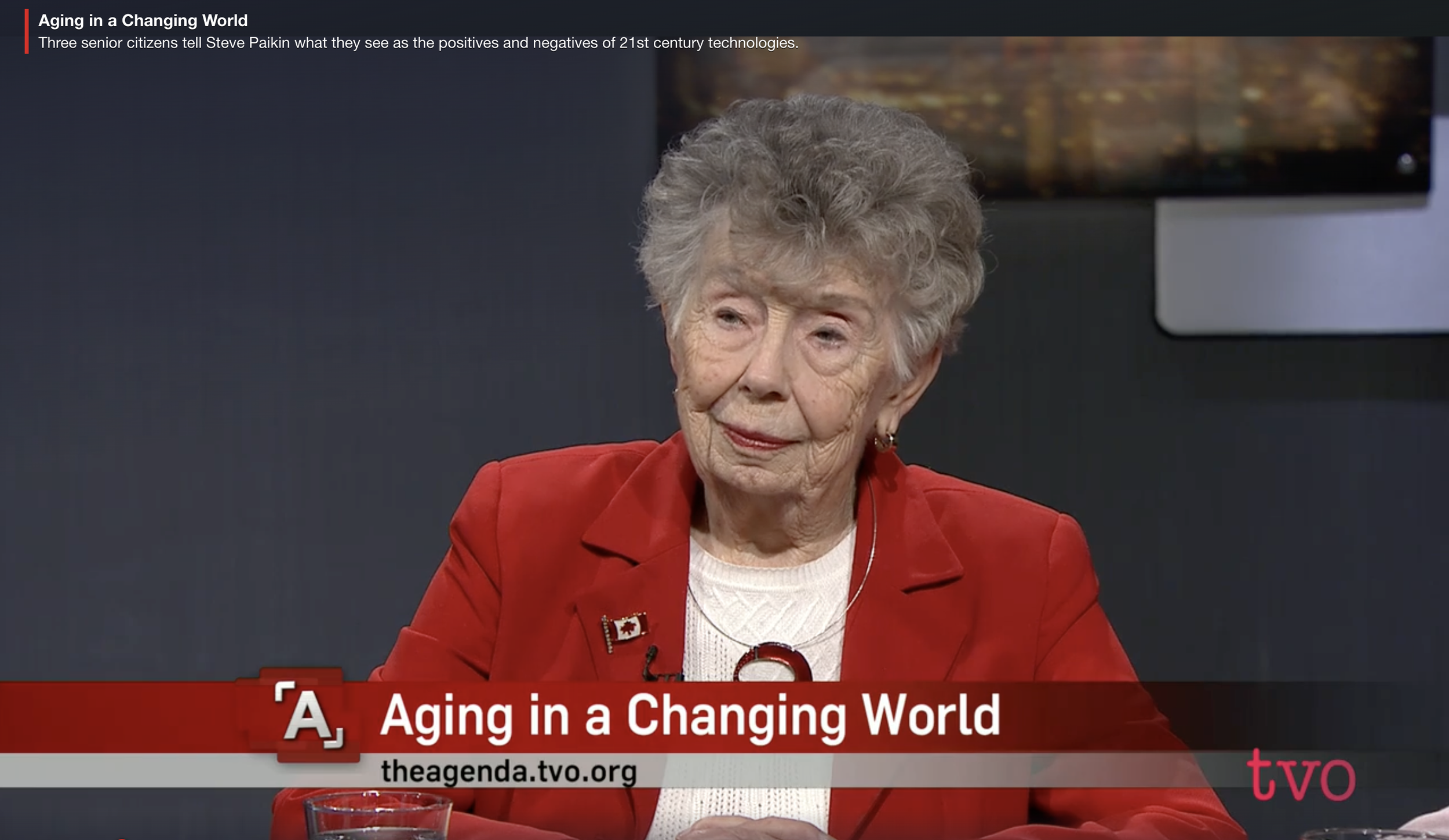 Image of an older woman wearing a bright red blazer on a television program with the caption "Aging in a Changing World".