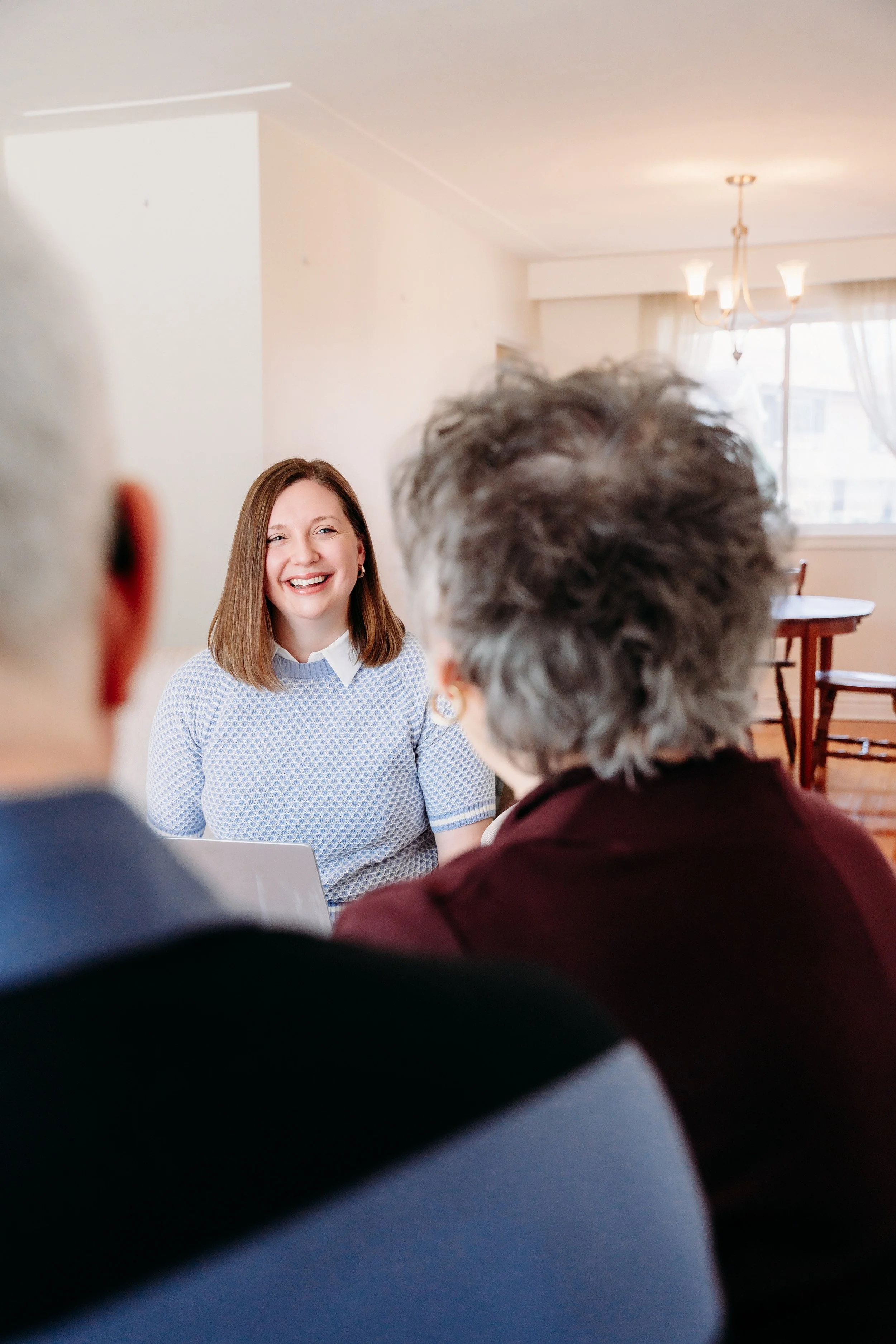 A woman smiling during a meeting with two older individuals in a home setting.