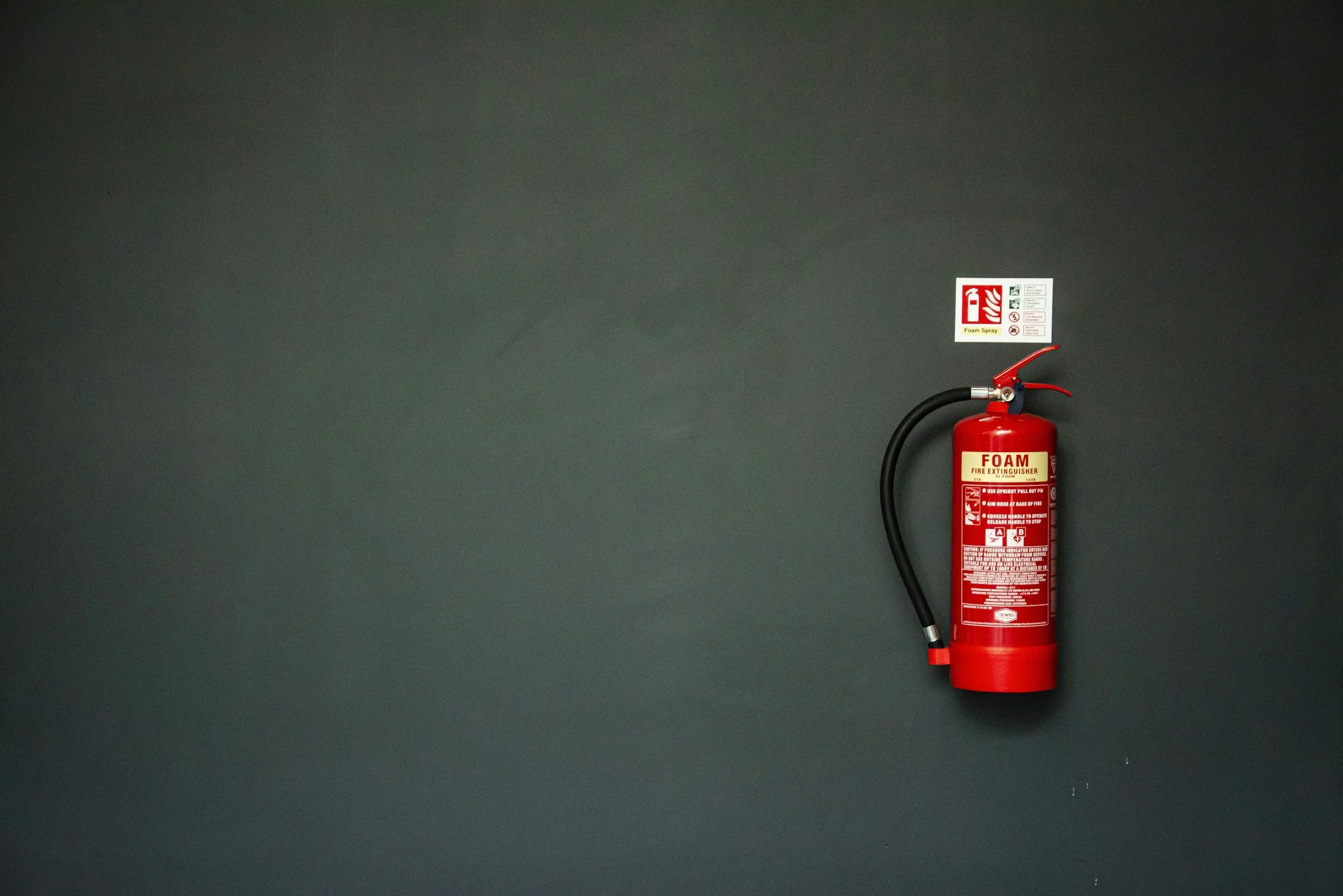 Red fire extinguisher mounted on a dark wall, with a safety instruction sticker above it.