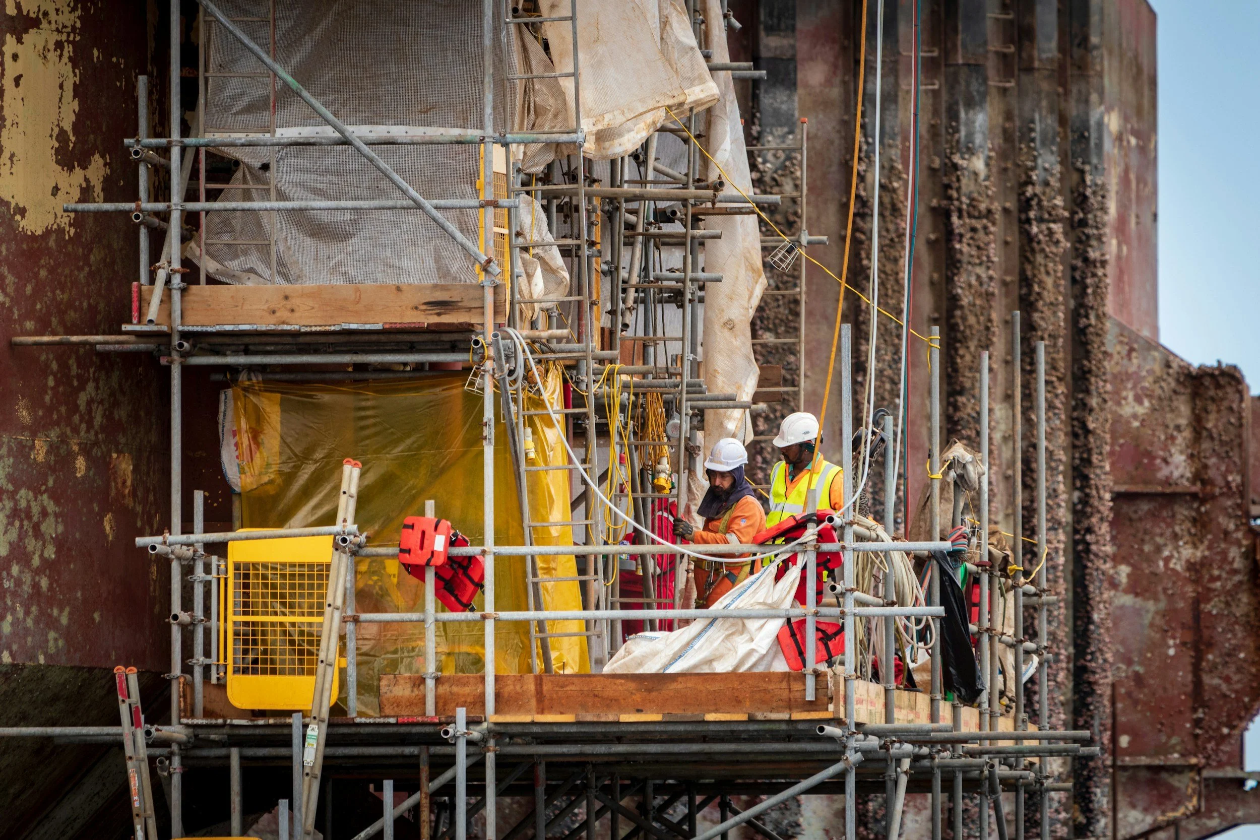 Construction workers wearing safety gear working on scaffolding on a building with a weathered exterior.