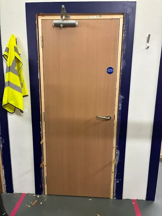 A closed wooden door with a silver handle, mounted on a black and white wall, with construction or repair work around the edges.