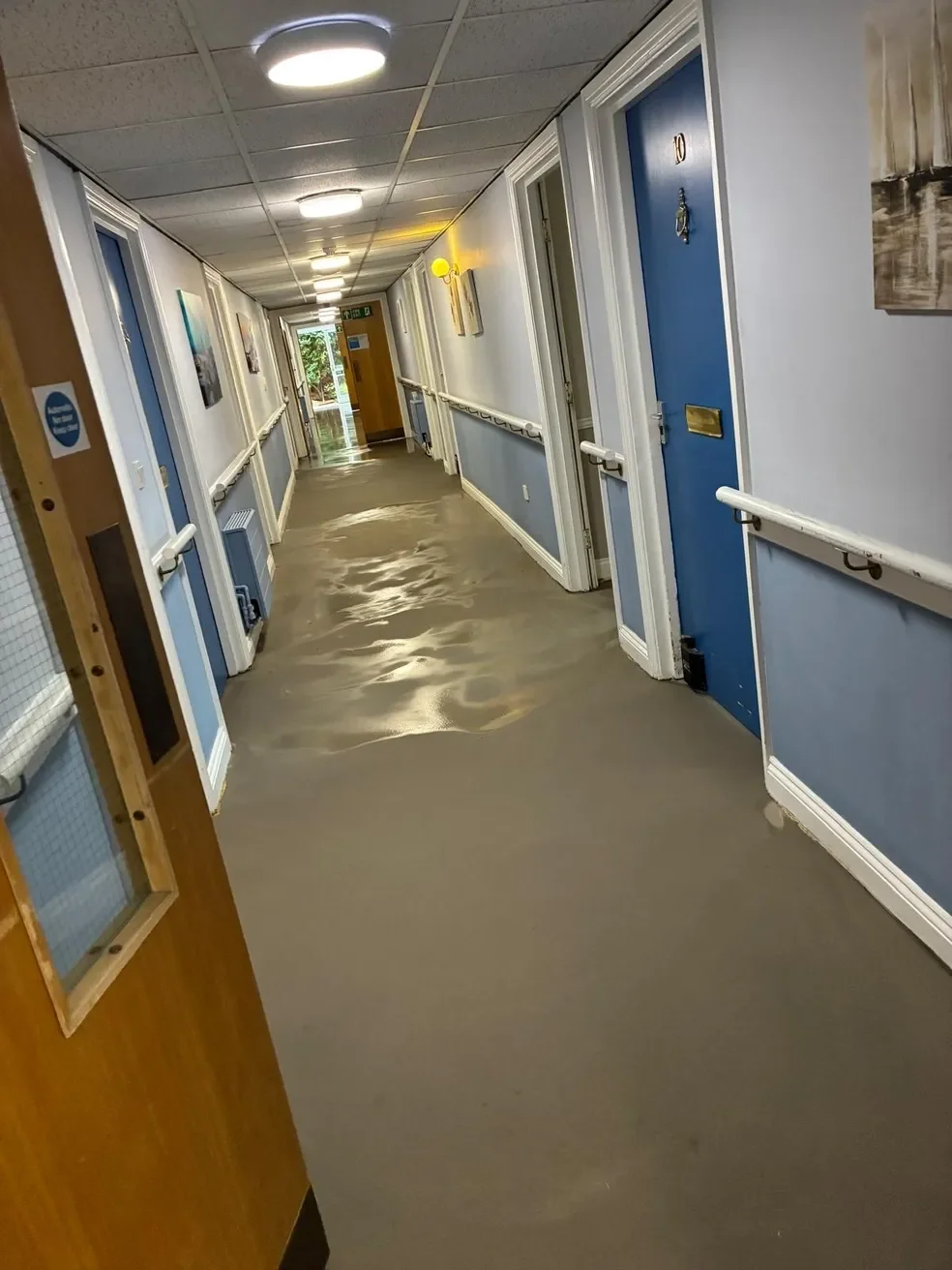 Nursing home hallway with orange flooring and blue doors, with water spilled across the floor.