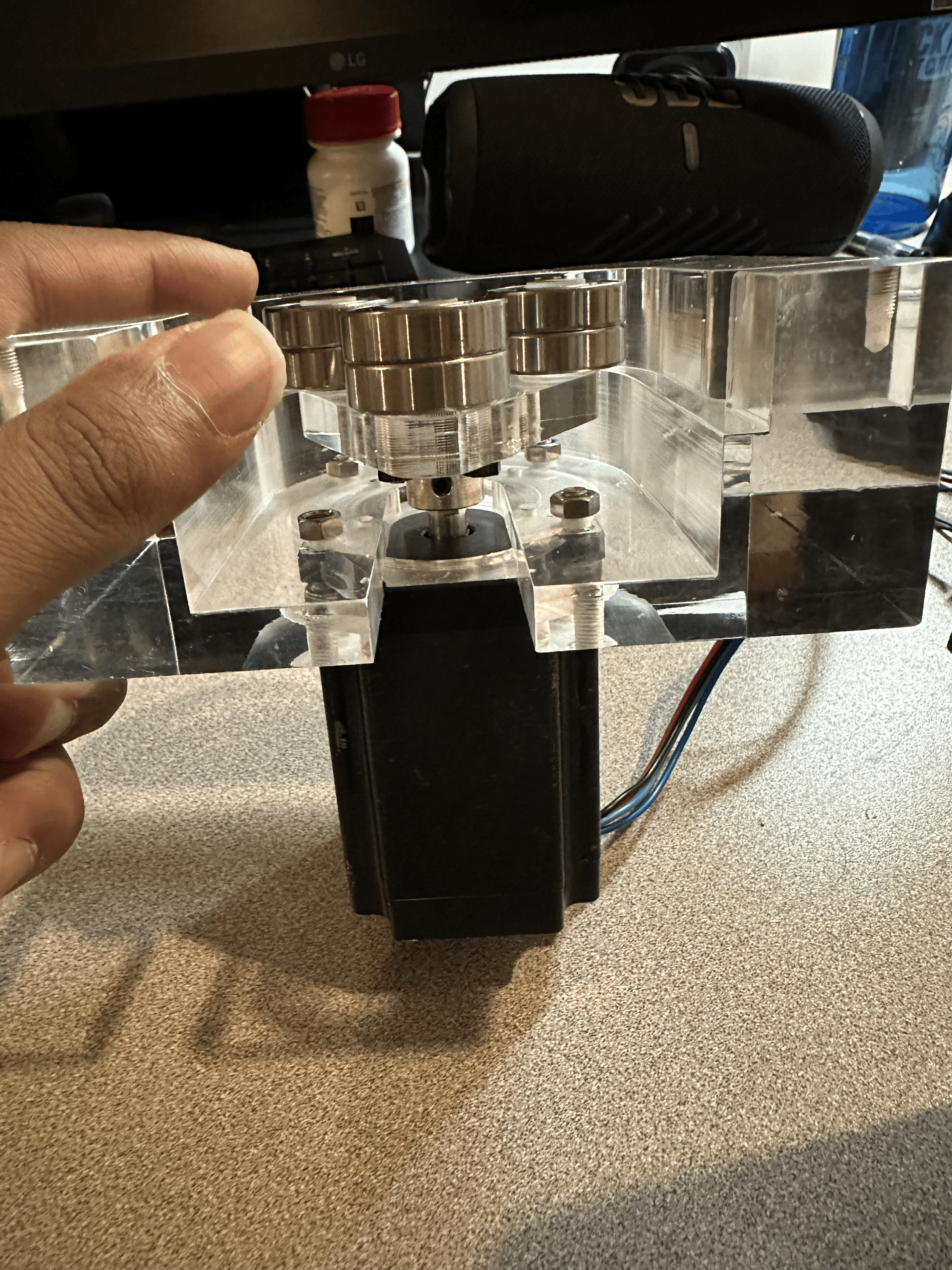 A person holding a clear acrylic and metal precision machine part with screws and a motor on a beige desk.