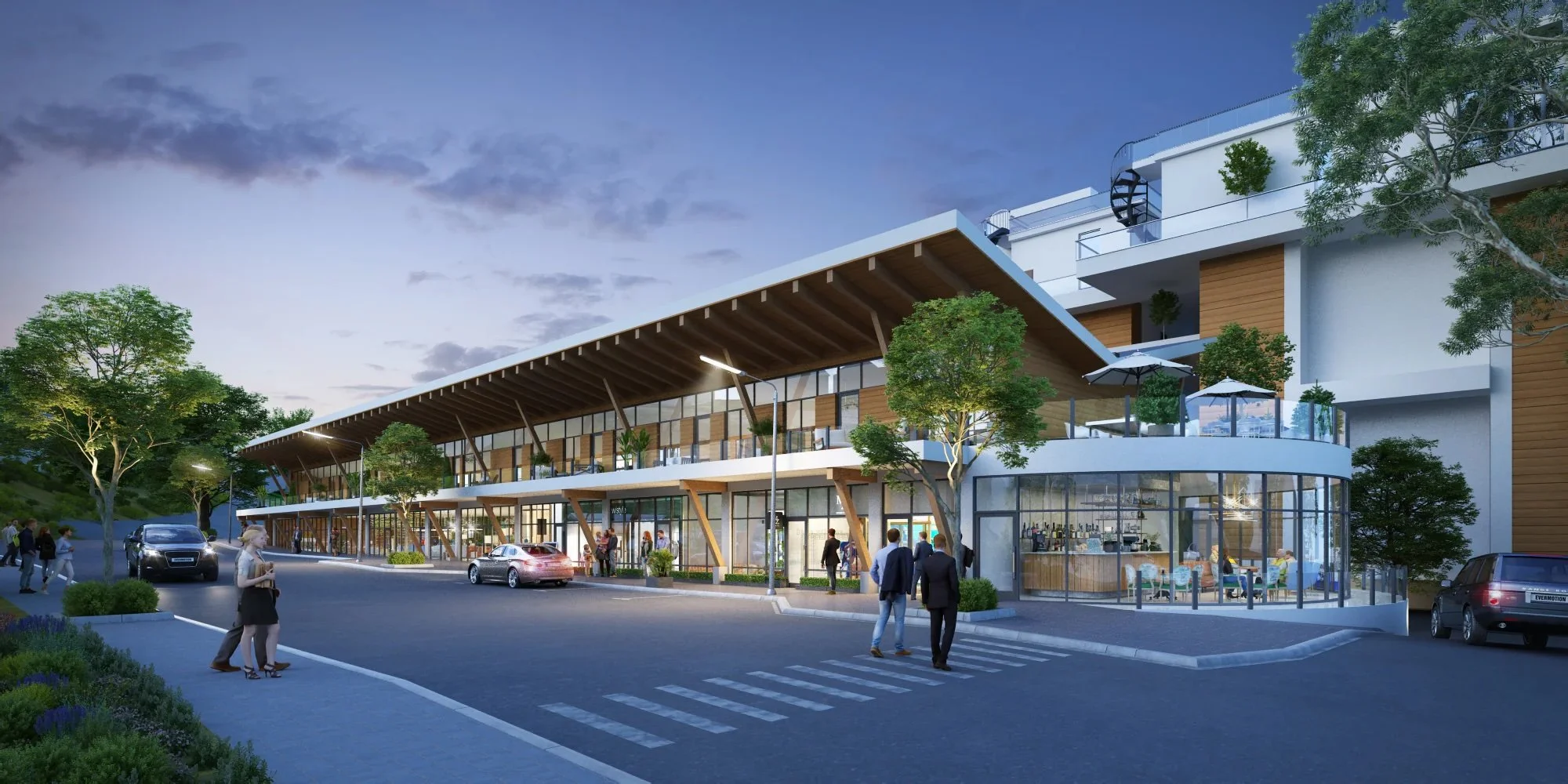 A modern multi-story building with large glass windows, balconies, and outdoor seating areas, surrounded by trees and cars, under a partly cloudy sky at dusk.