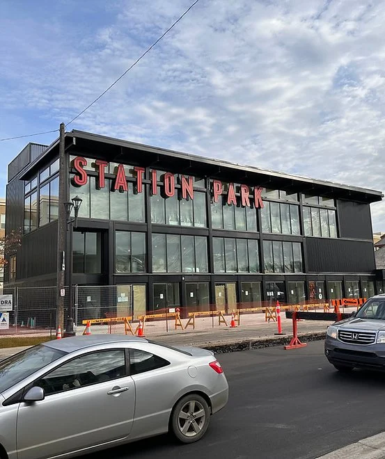 Modern building labeled 'Station Park' with large glass windows, construction cones, and parked cars in front.