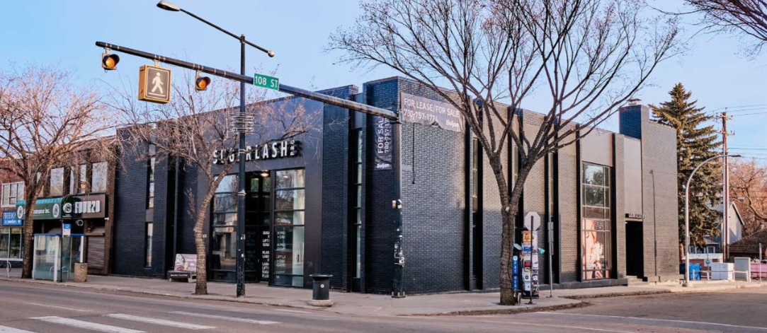 Modern black brick building on a city street with leafless trees, street signs, and traffic lights.