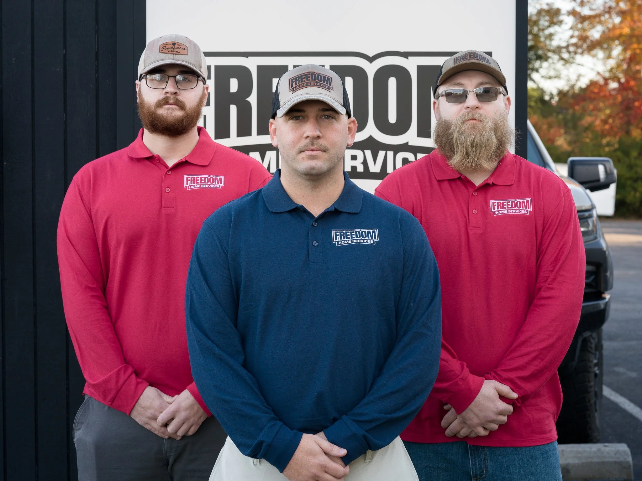 Three men standing in front of a vehicle with a sign that reads 'Freedom Home Services'; one is wearing a blue shirt, and two are wearing red shirts, all with the company's logo.