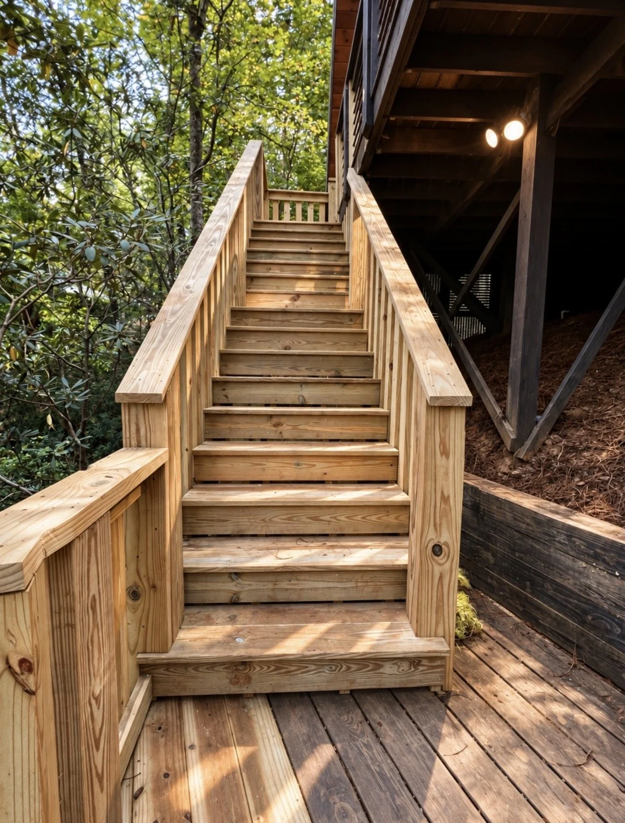 Wooden outdoor staircase leading to an upper deck, surrounded by trees and greenery.