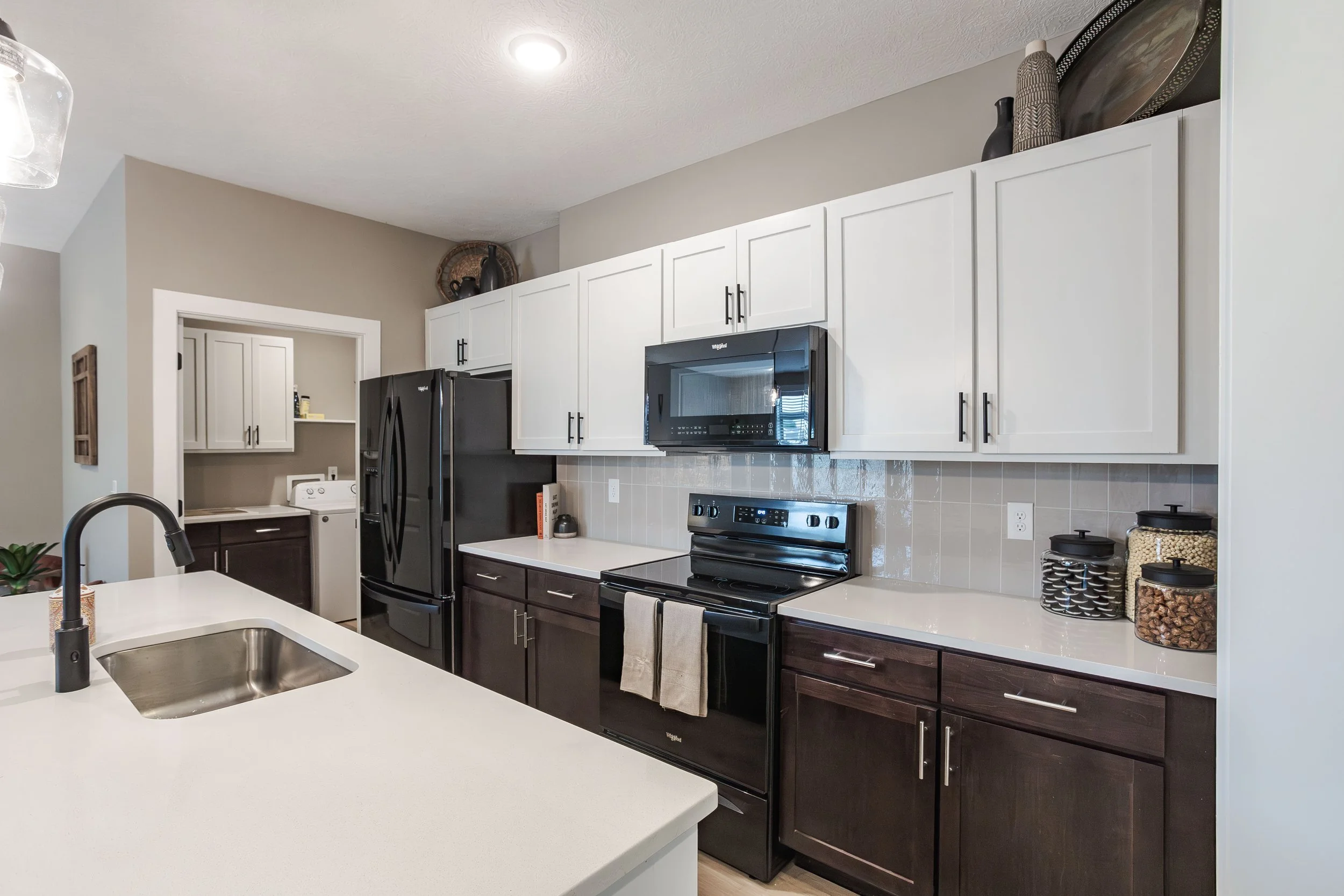 Modern kitchen with white upper cabinets, dark lower cabinets, black appliances, and a white countertop island with a sink.
