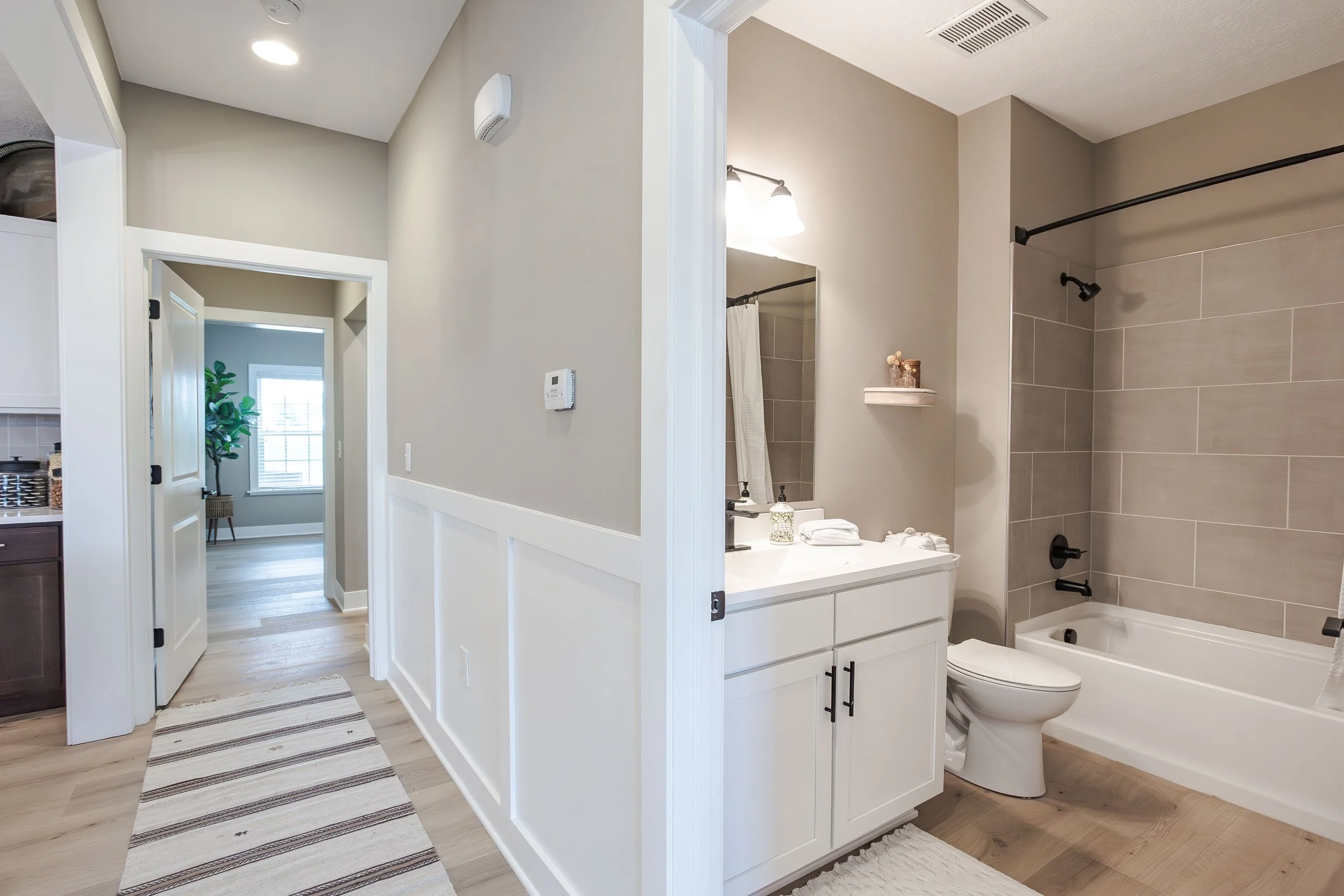 Bathroom with white vanity, mirror, towel, and bathtub with beige tiles, seen from hallway