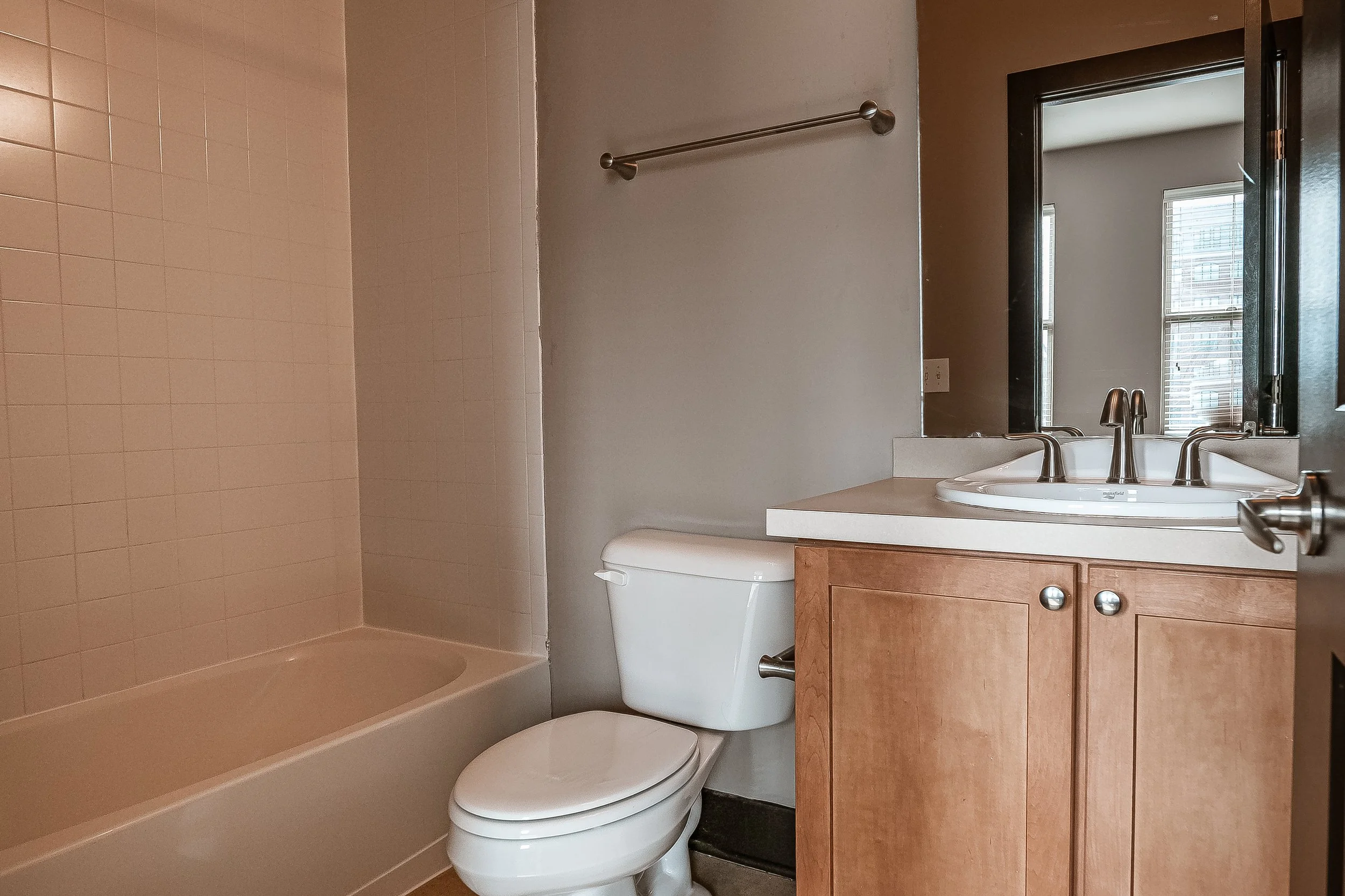 Bathroom with bathtub, toilet, and wooden vanity with sink, mirror, and window.