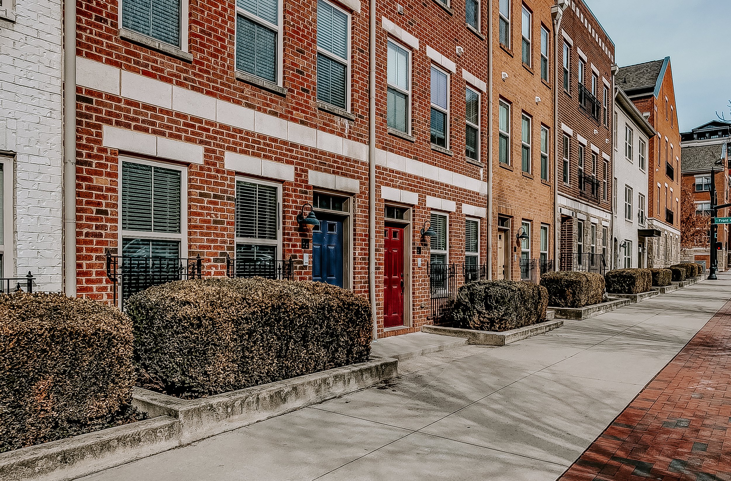 Row of modern brick townhouses along a sidewalk, with hedges in front and a street sign at the corner in Downtown Columbus, OH