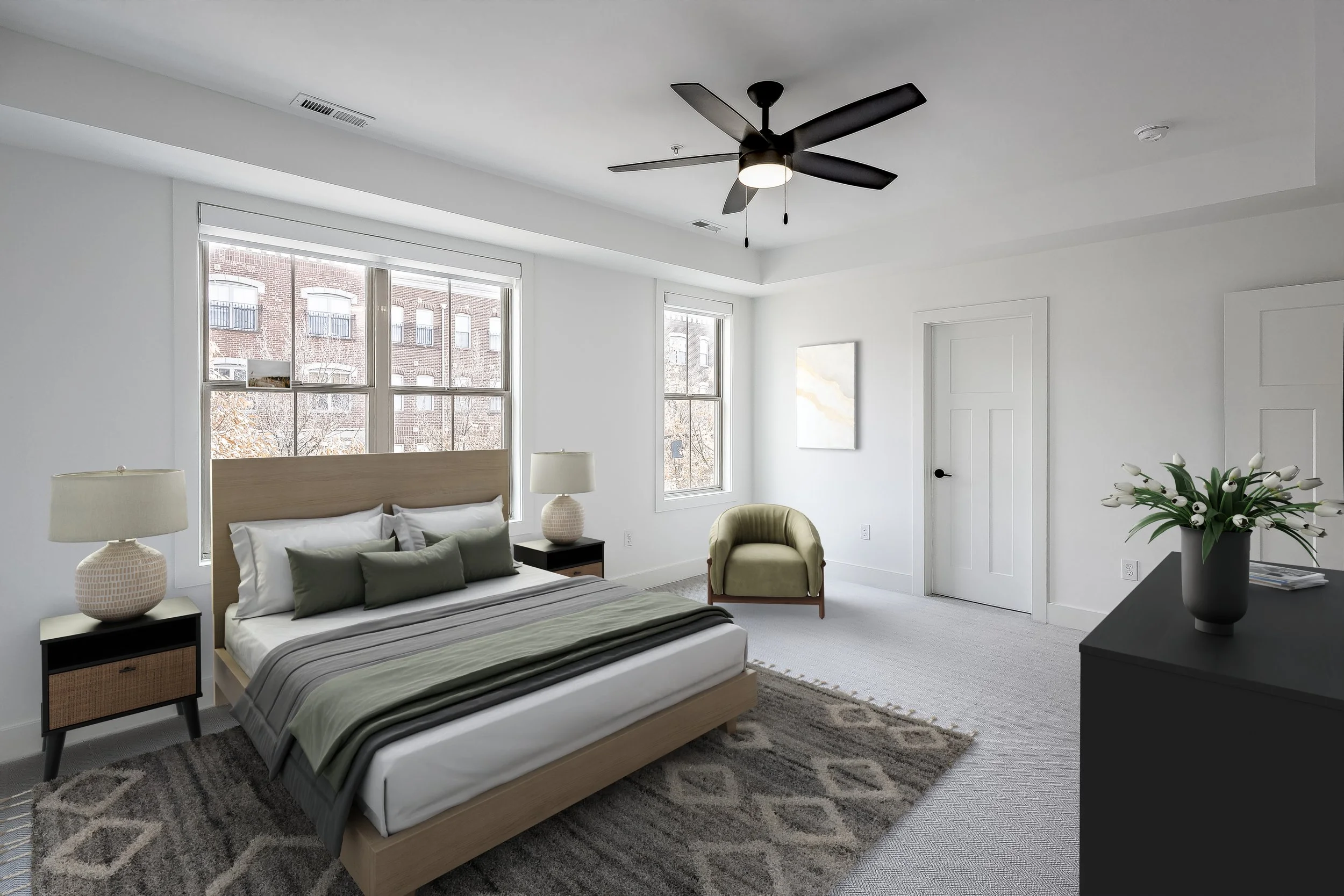 A modern bedroom with a bed, nightstands, lamps, a green armchair, a black dresser with a flower vase, and windows showing outside buildings.