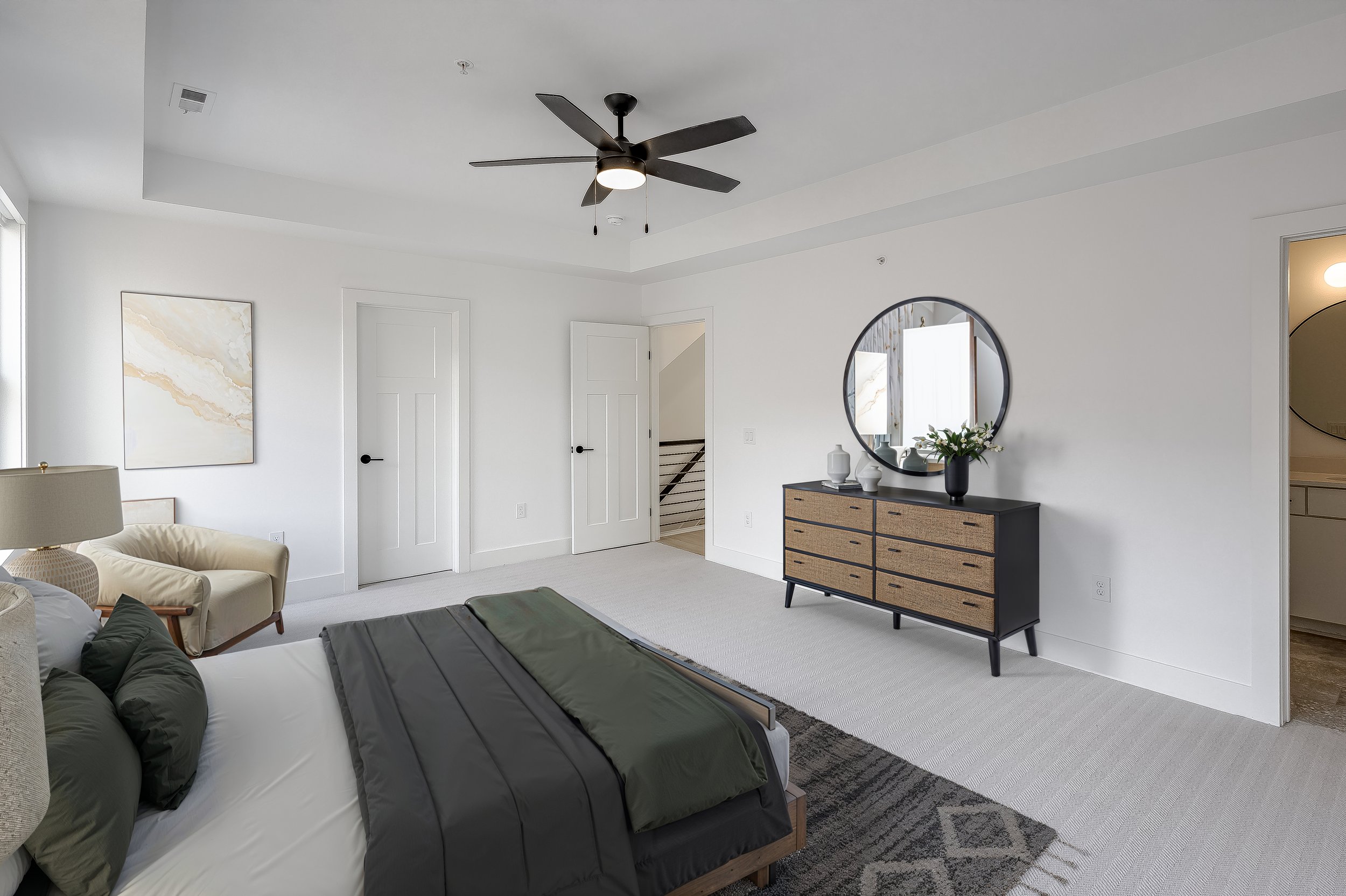 Modern bedroom with white walls, black ceiling fan, dresser, mirror, bed with black and green bedding, and beige chairs.