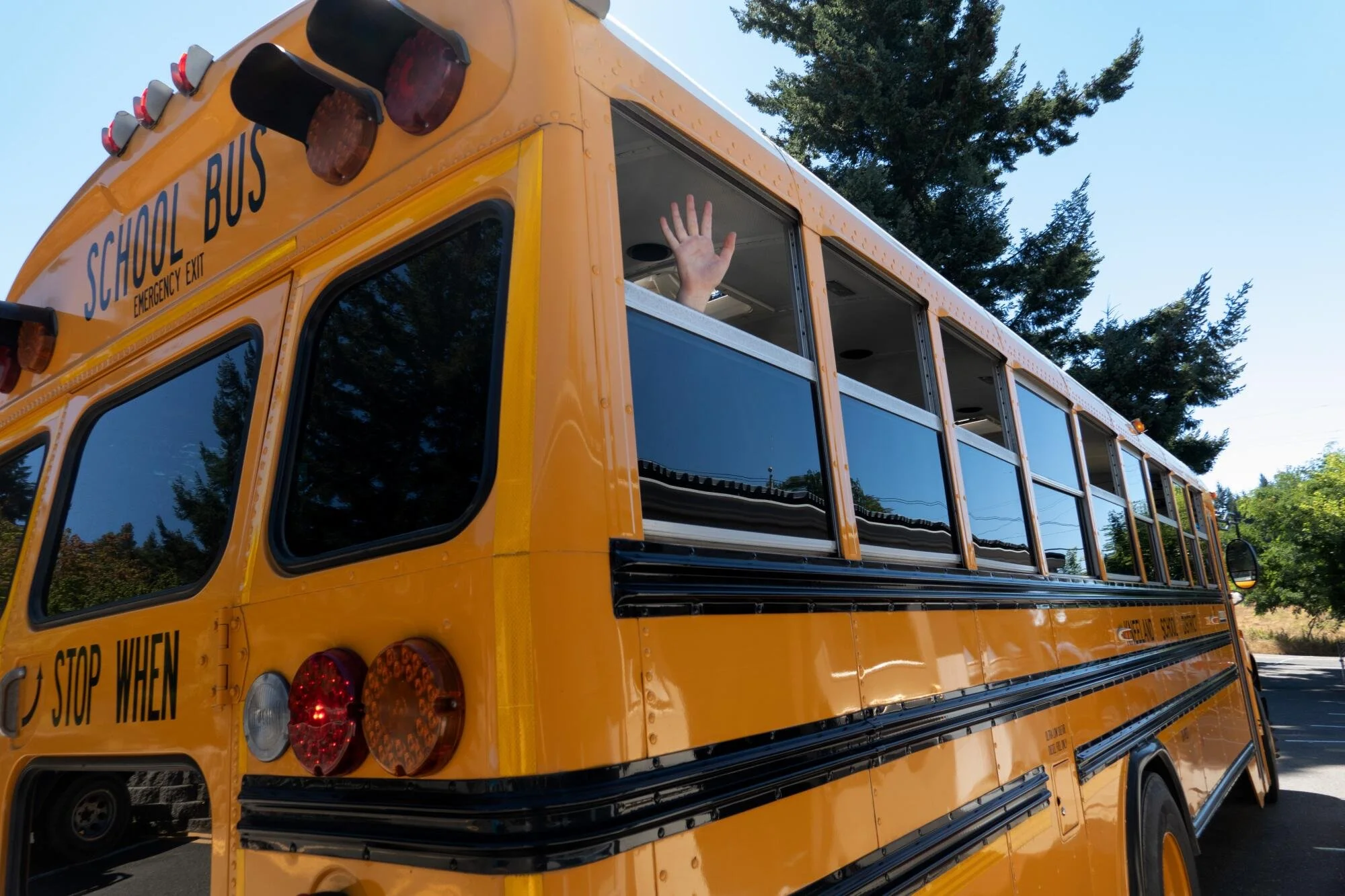 A yellow school bus with an open window, and a person waving their hand outside.
