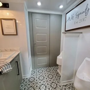 A compact bathroom with a gray door, patterned black-and-white floor tiles, a white wall-mounted toilet, a framed quote about equality, and a partial view of a sink countertop with a checkered towel.