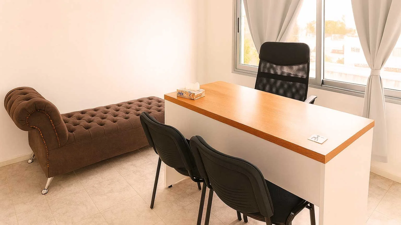 Una sala de oficina con un escritorio, tres sillas negras, un diván marrón y una ventana con cortinas blancas.