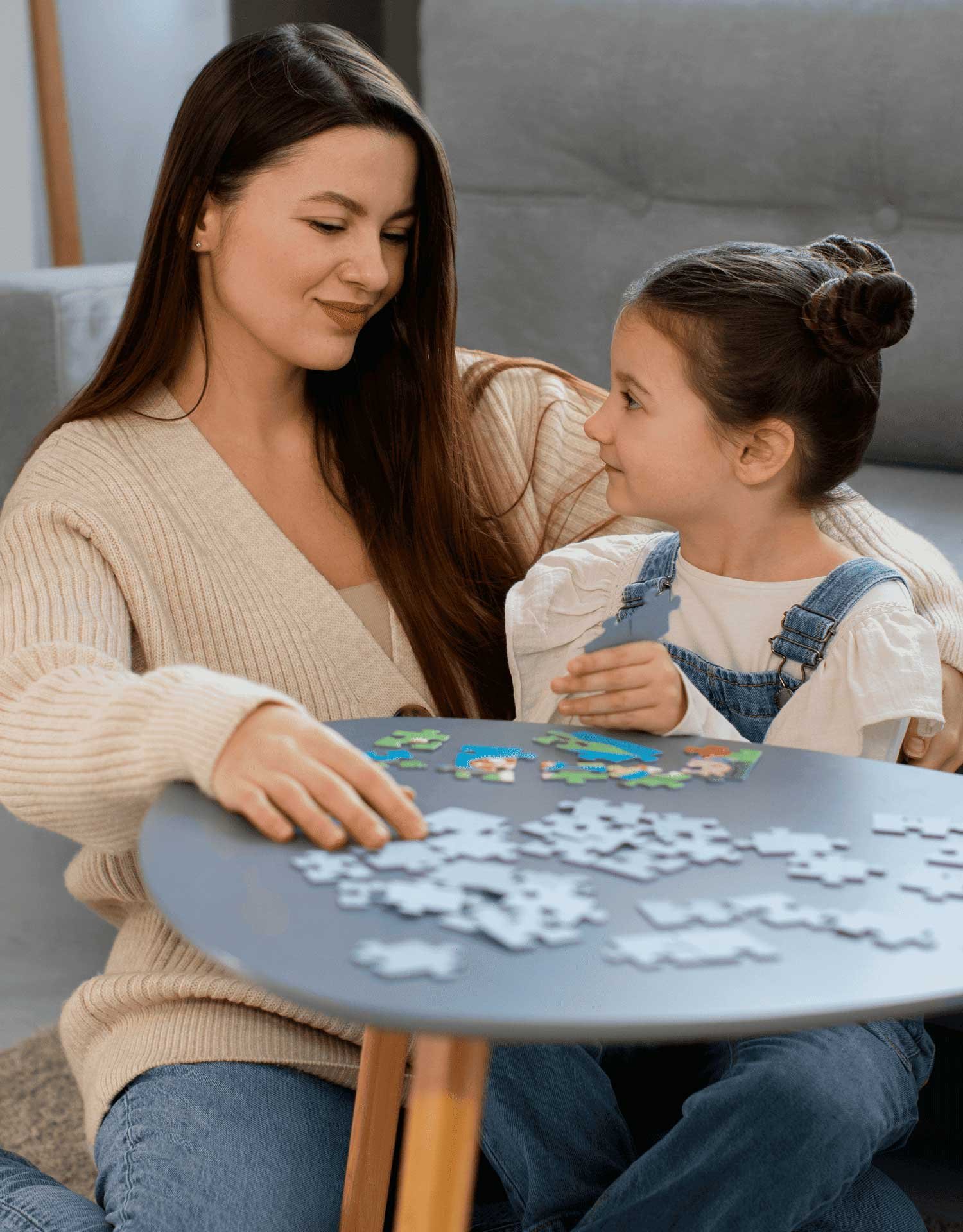 Una mujer y una niña se sientan en una mesa pequeña y arman rompecabezas juntas en una acogedora sala de estar.