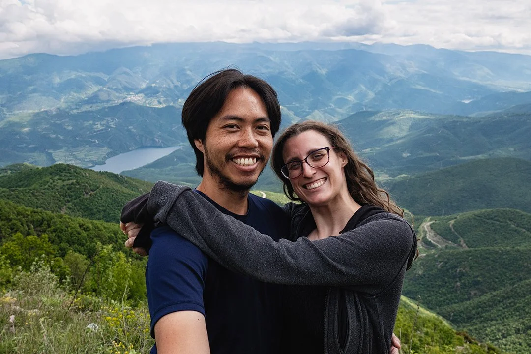 Smiling couple hugging on a mountain with green hills and a lake in the background