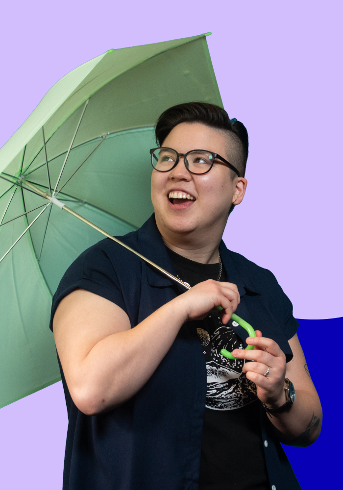 A person with short dark hair, glasses, and a nose ring holding a light green umbrella and smiling.