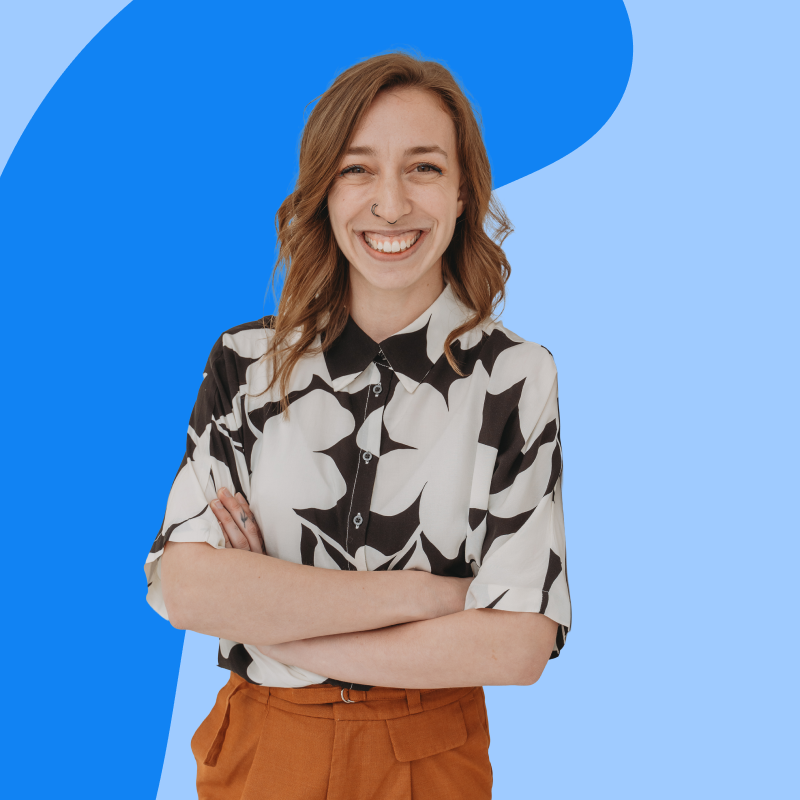 Smiling person with crossed arms, wearing a black and white patterned shirt and brown pants, against a blue abstract background.