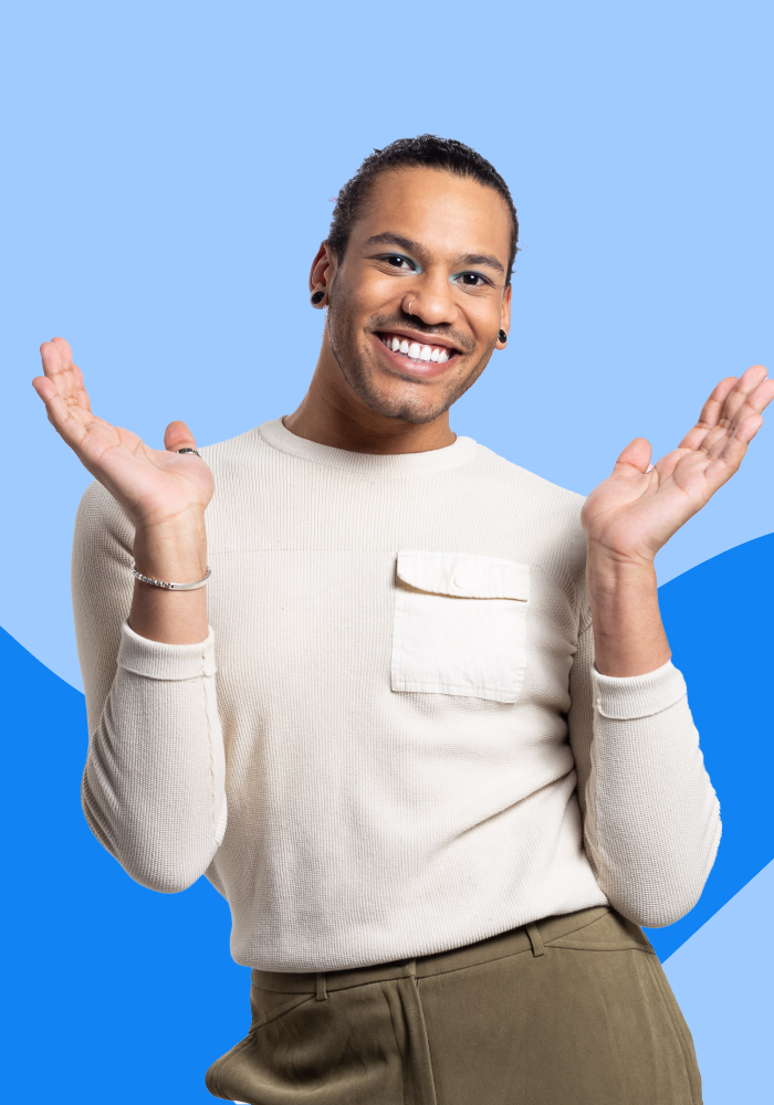 A smiling person with dark hair, earrings, and a nose ring raises both hands in a playful pose against a blue background.
