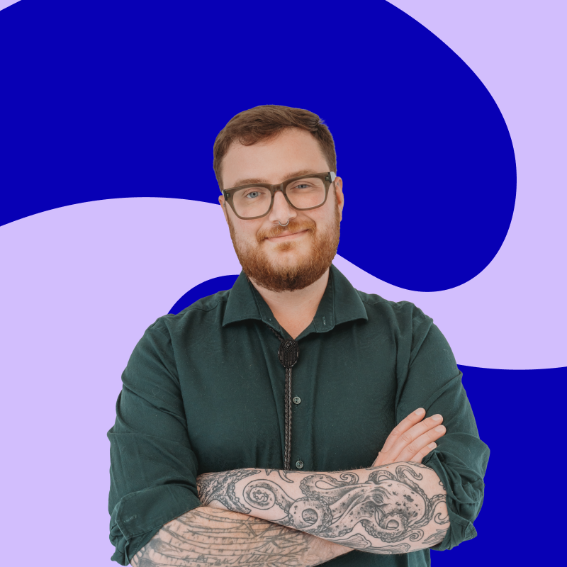 Portrait of a person with glasses and tattoos crossing their arms, standing in front of a blue and purple abstract background.