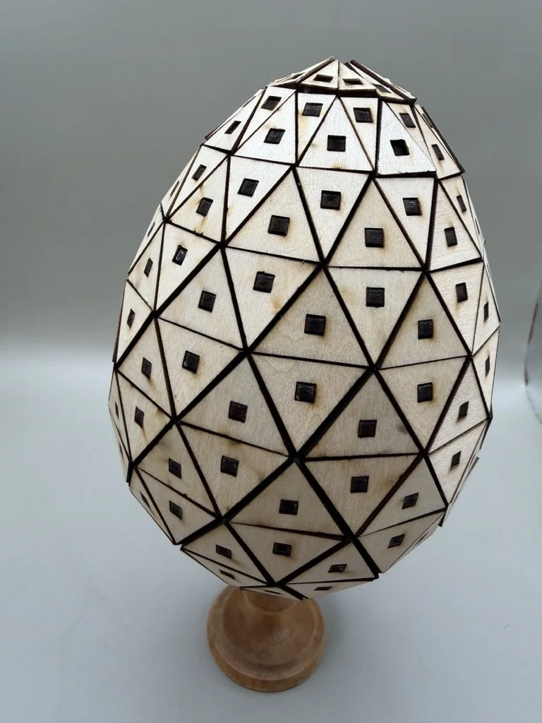 Decorative wooden egg-shaped object with geometric patterns on a small wooden stand.