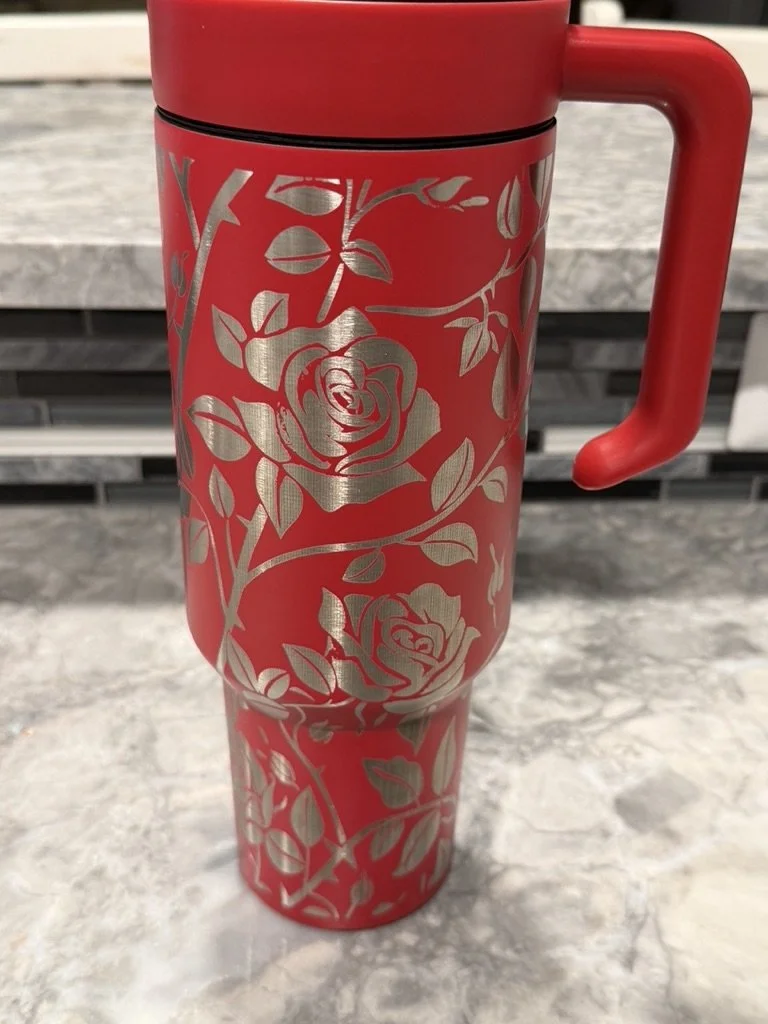 Red travel mug with a floral rose pattern in silver, positioned on a marble countertop.