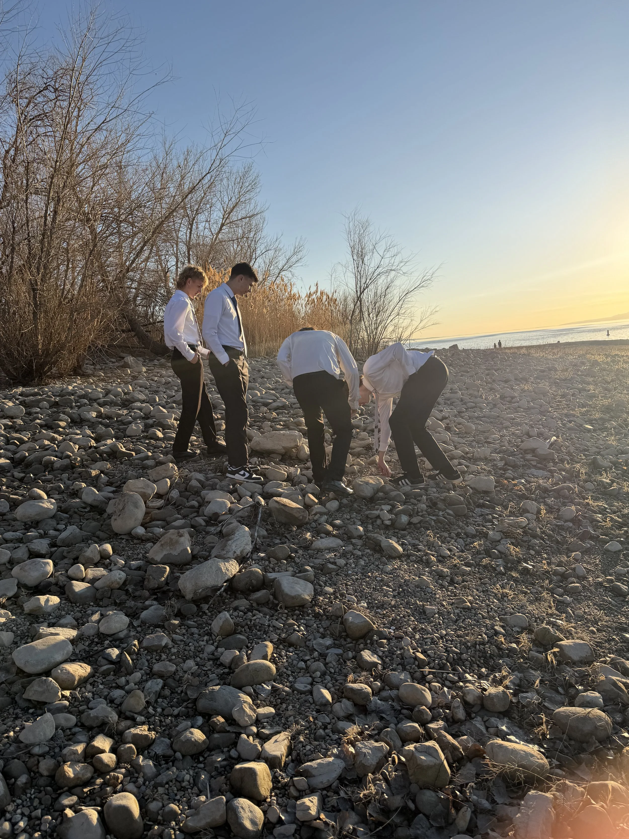 Four people in formal attire examining rocks on a rocky beach at sunset.