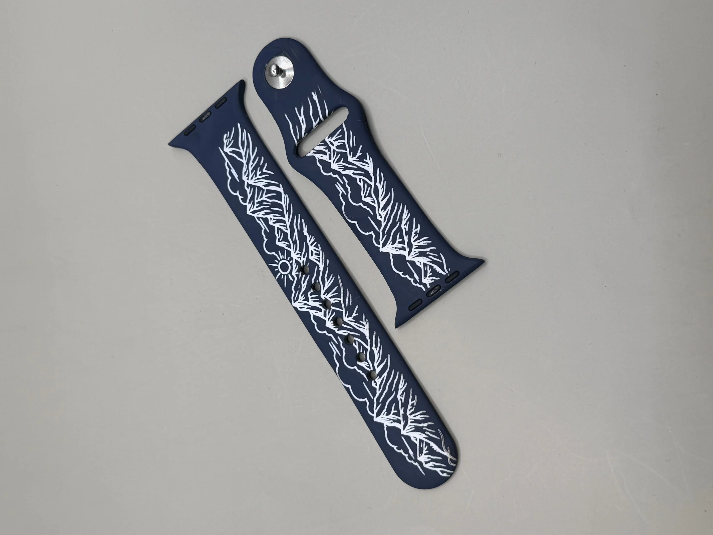 Navy silicone Apple Watch band laser-engraved with a white mountain range, clouds, and sunrise design