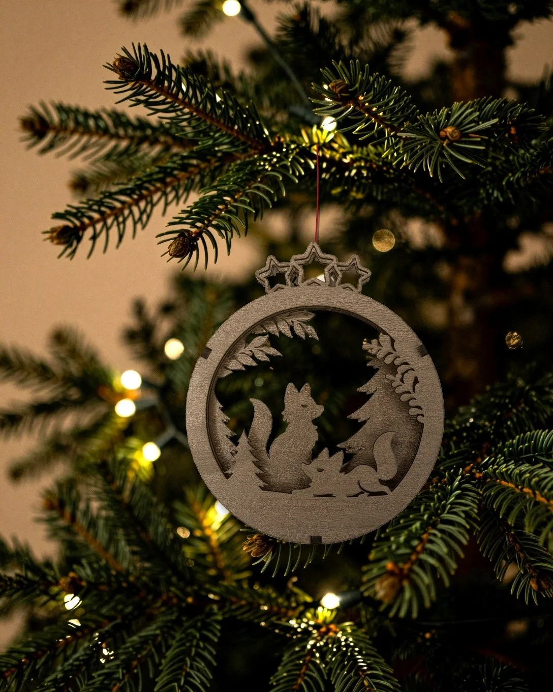 Walnut fox layered wood Christmas ornament hanging on a fir tree with warm string lights