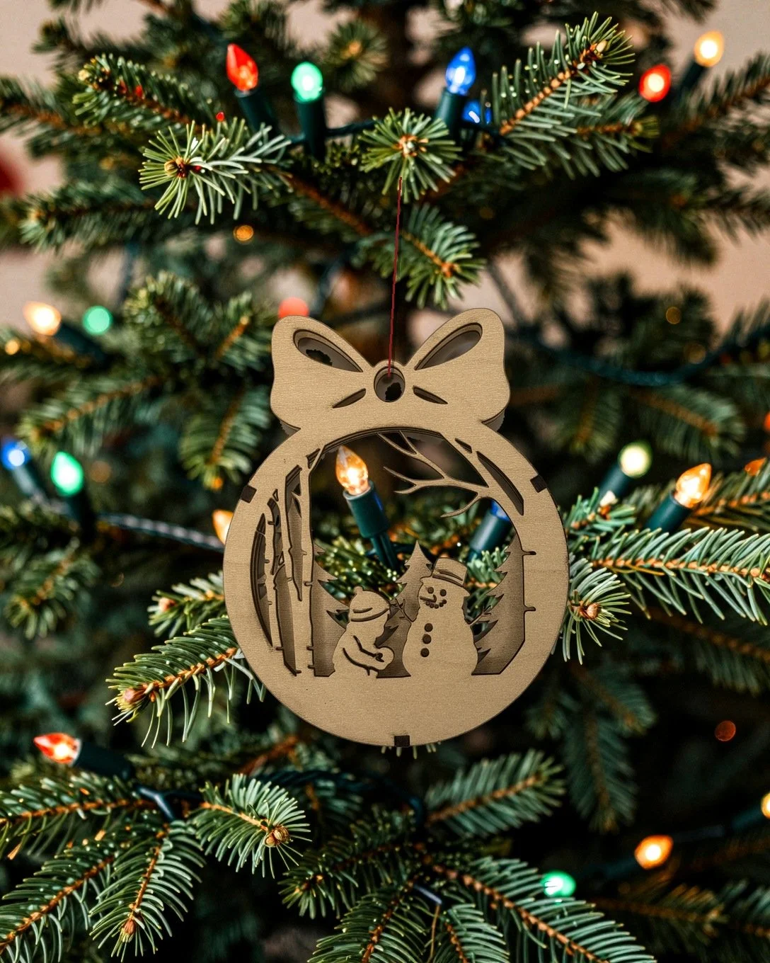 Maple child and snowman layered wood Christmas ornament hanging on a tree with vintage colored lights