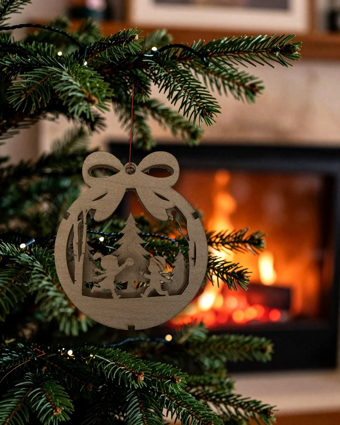 Walnut Christmas elves layered wood ornament hanging on a tree beside a fireplace