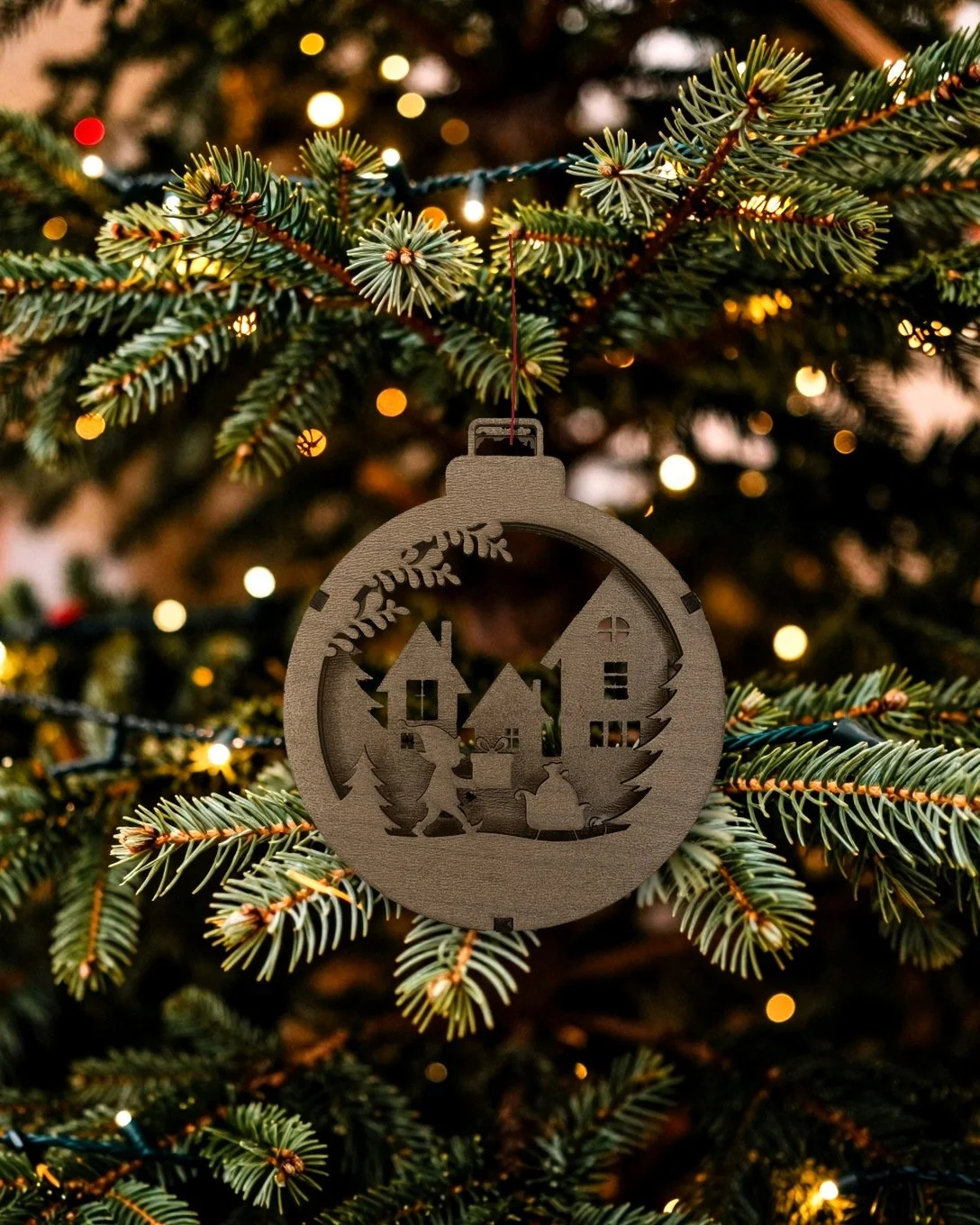 Walnut Christmas village layered wood ornament hanging on a tree with golden lights