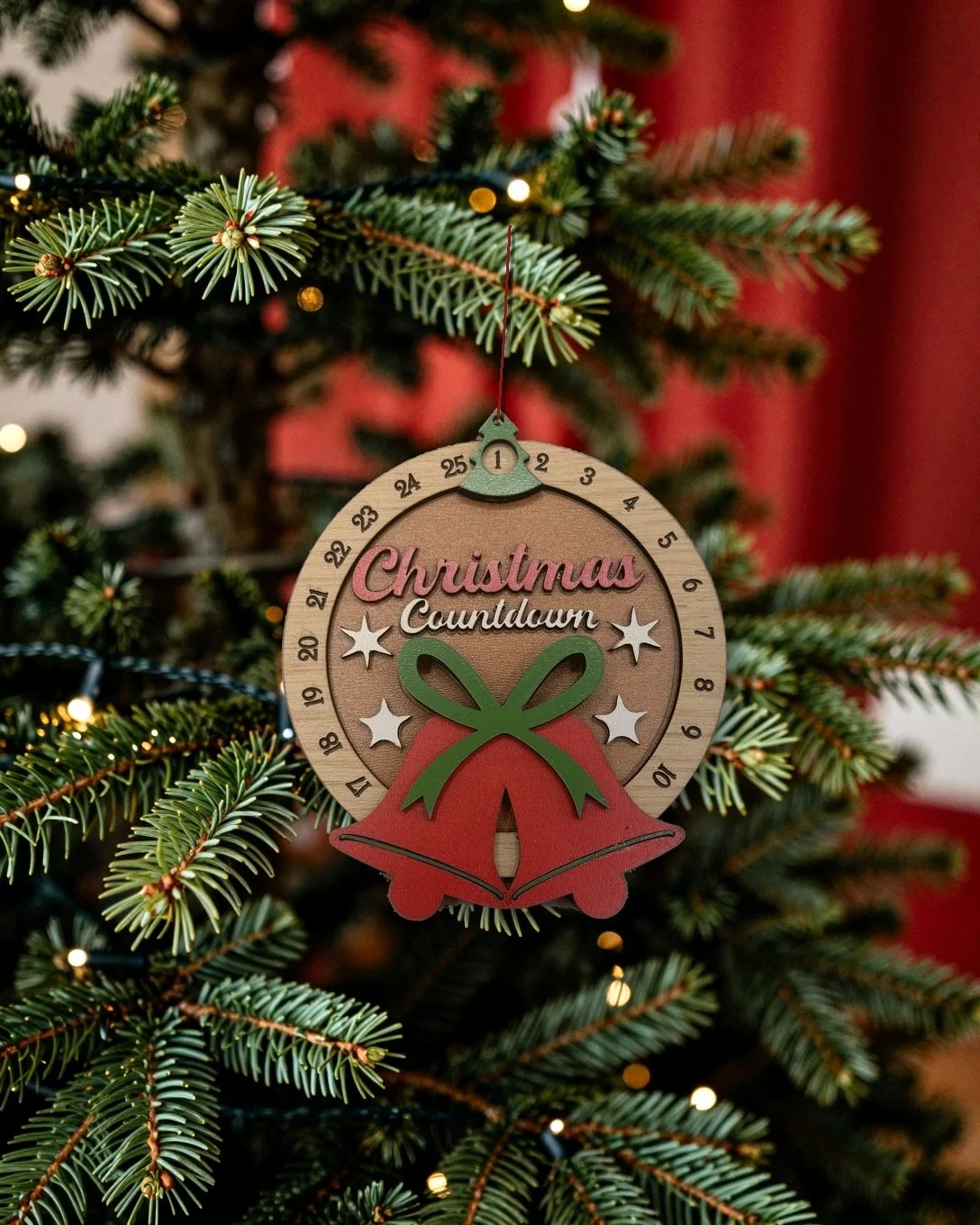 Hand-painted Christmas countdown ornament with red bells hanging on a Christmas tree