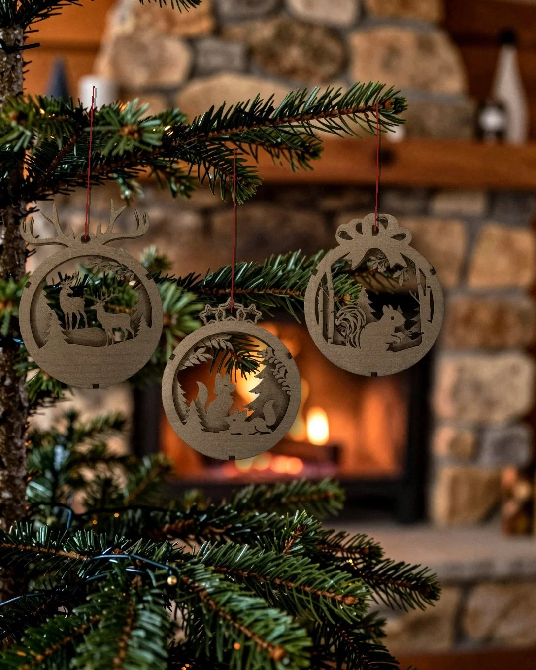 Woodland Animals 3-pack of walnut layered wood ornaments hanging on a tree by a stone fireplace