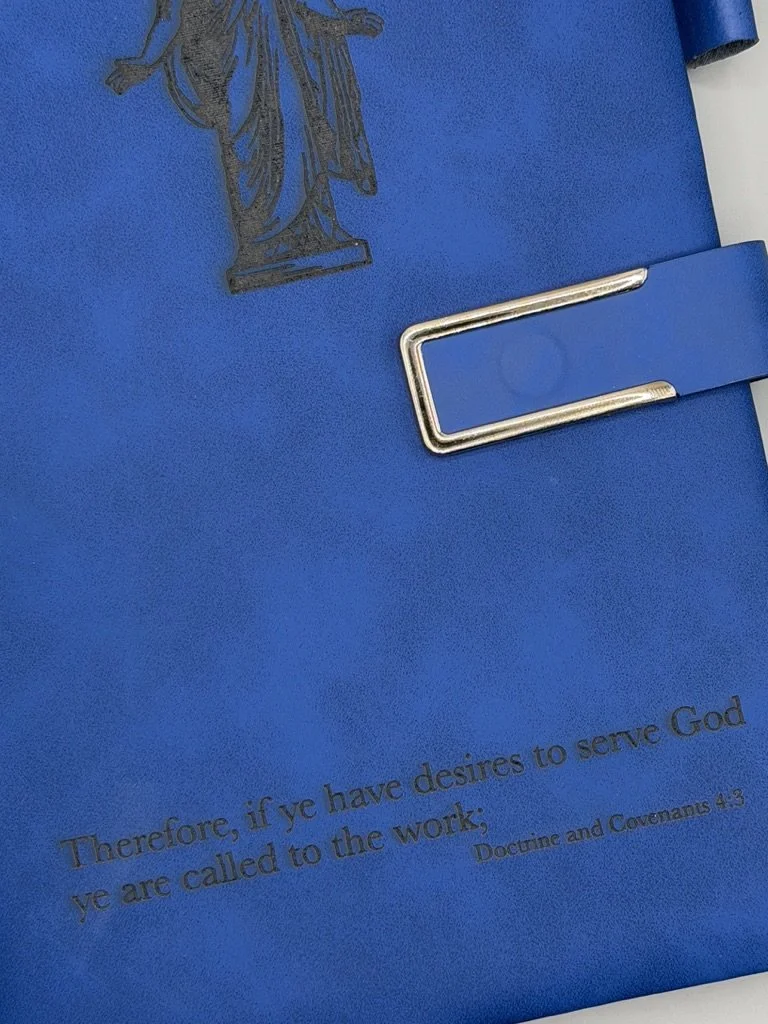 Blue booklet with a metallic metal clip and a black silhouette of the Statue of Liberty in the top left corner. A Bible verse is partially visible at the bottom, reading: "Therefore, if ye have desires to serve God ye are called to the work;" from Do
