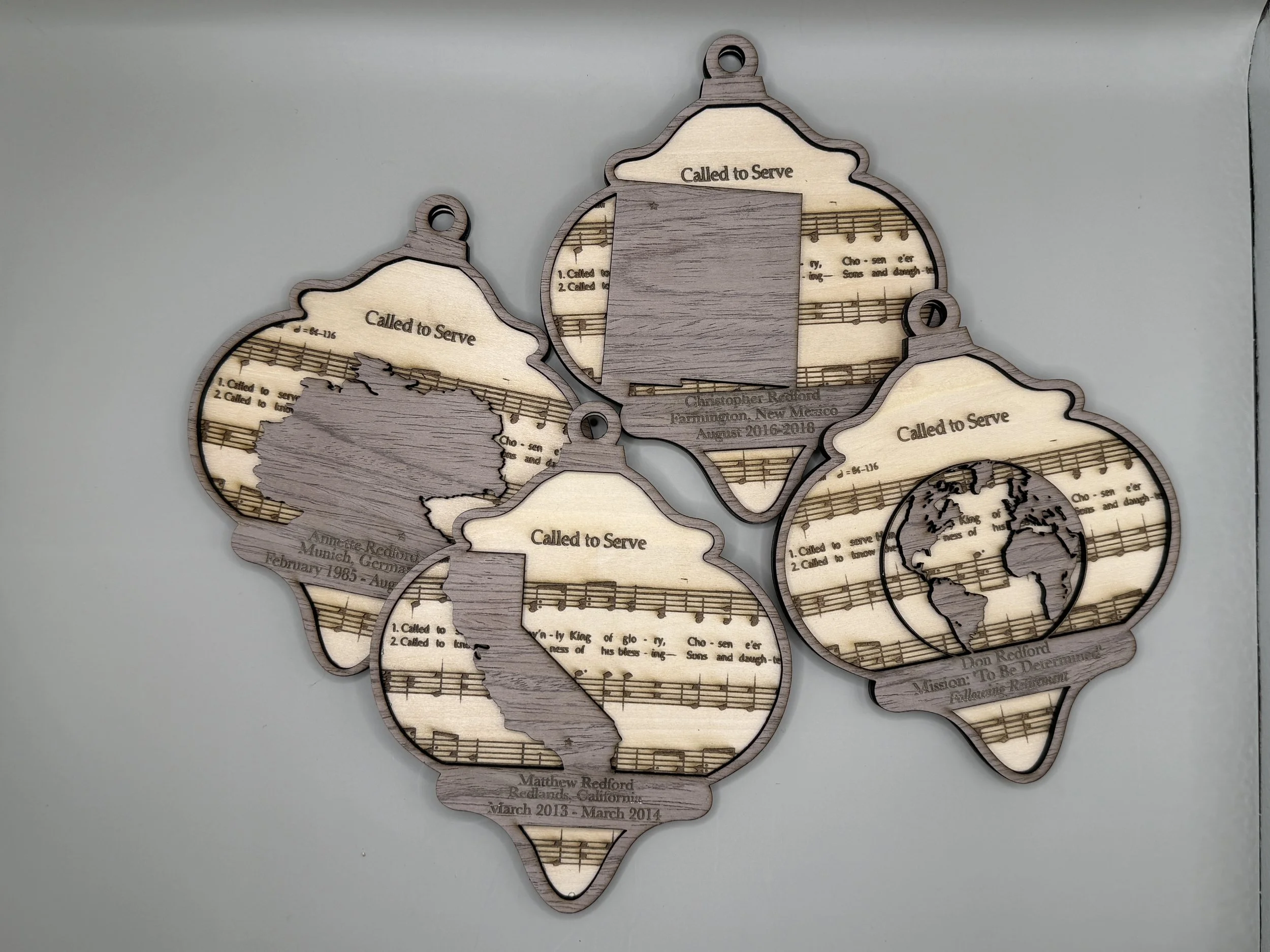 Decorative wooden plaques with musical notes, world map, and text that says 'Called to Serve' with personal information, worn for religious service memorials.