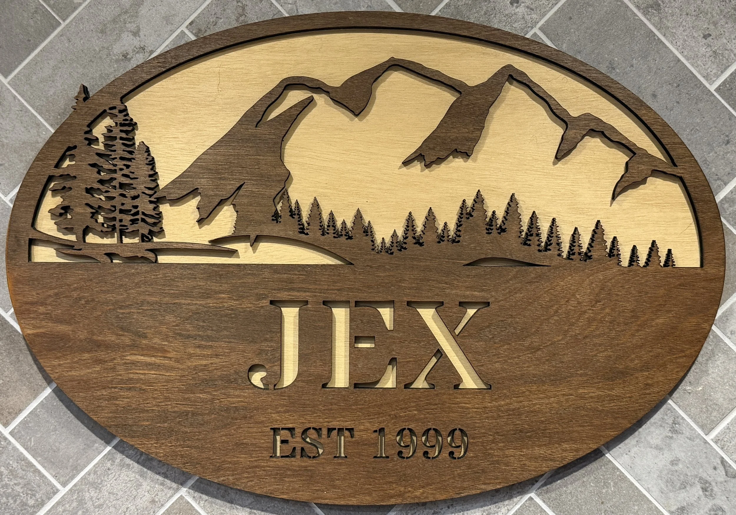 Wooden wall art with mountain, trees, and landscape design, featuring the text 'JEX' and 'EST 1999'.