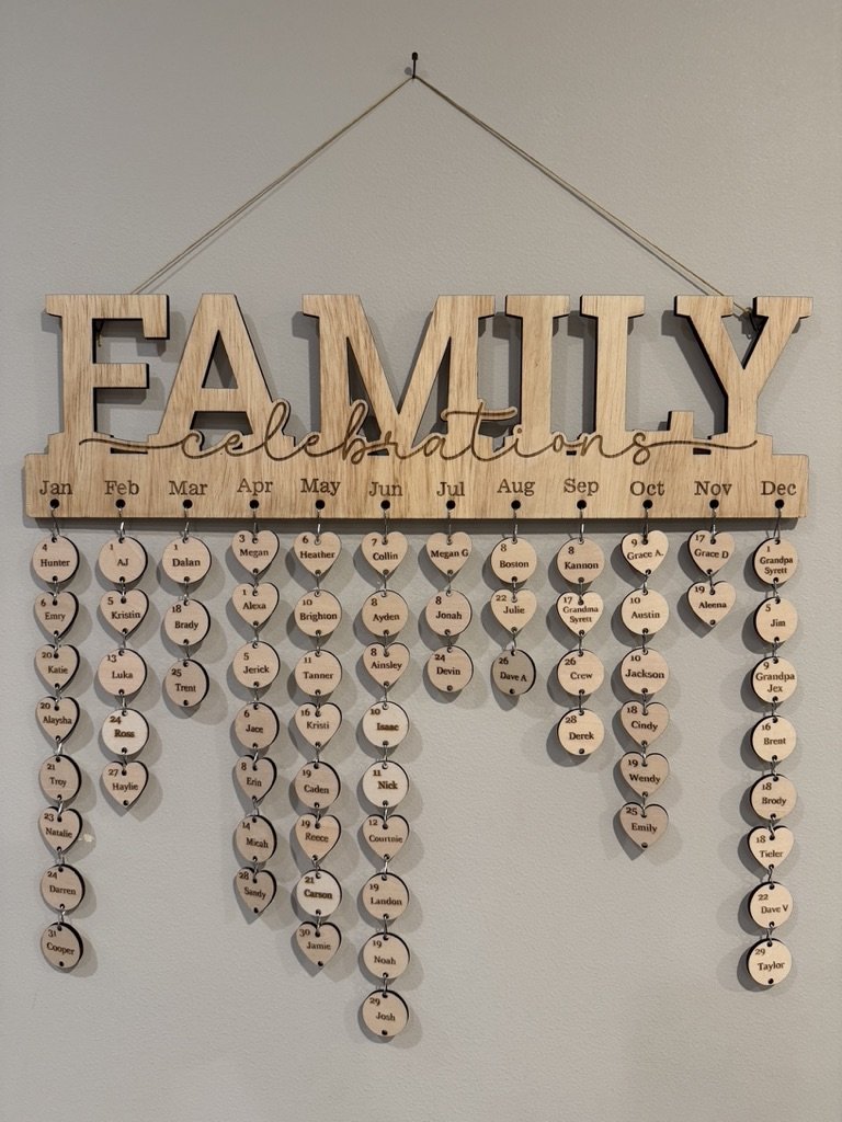 Wooden family tree display with the title 'Family Celebrations' and months of the year, showing names of family members on hanging circular discs connected by string.
