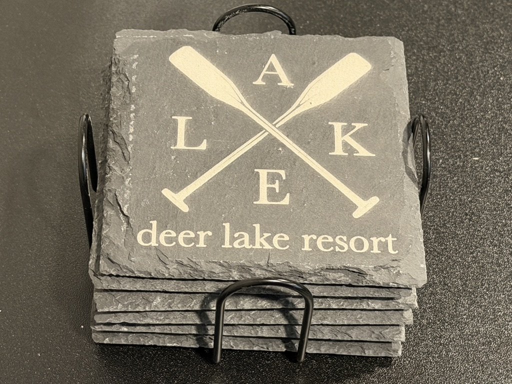 Stack of slate coasters with a logo of crossed oars and the word "LAKE" above and "deer lake resort" below.